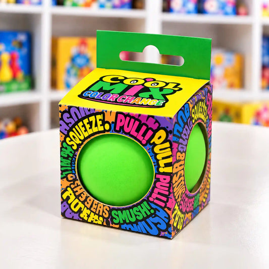 Cool Mix színváltós squishy stresszlevezető játék (zöld) – Élénkzöld stresszlabda színes, Cool Mix Color Change feliratú kartondobozban, kör alakú kivágásokkal, elmosódott játékbolti háttér előtt.