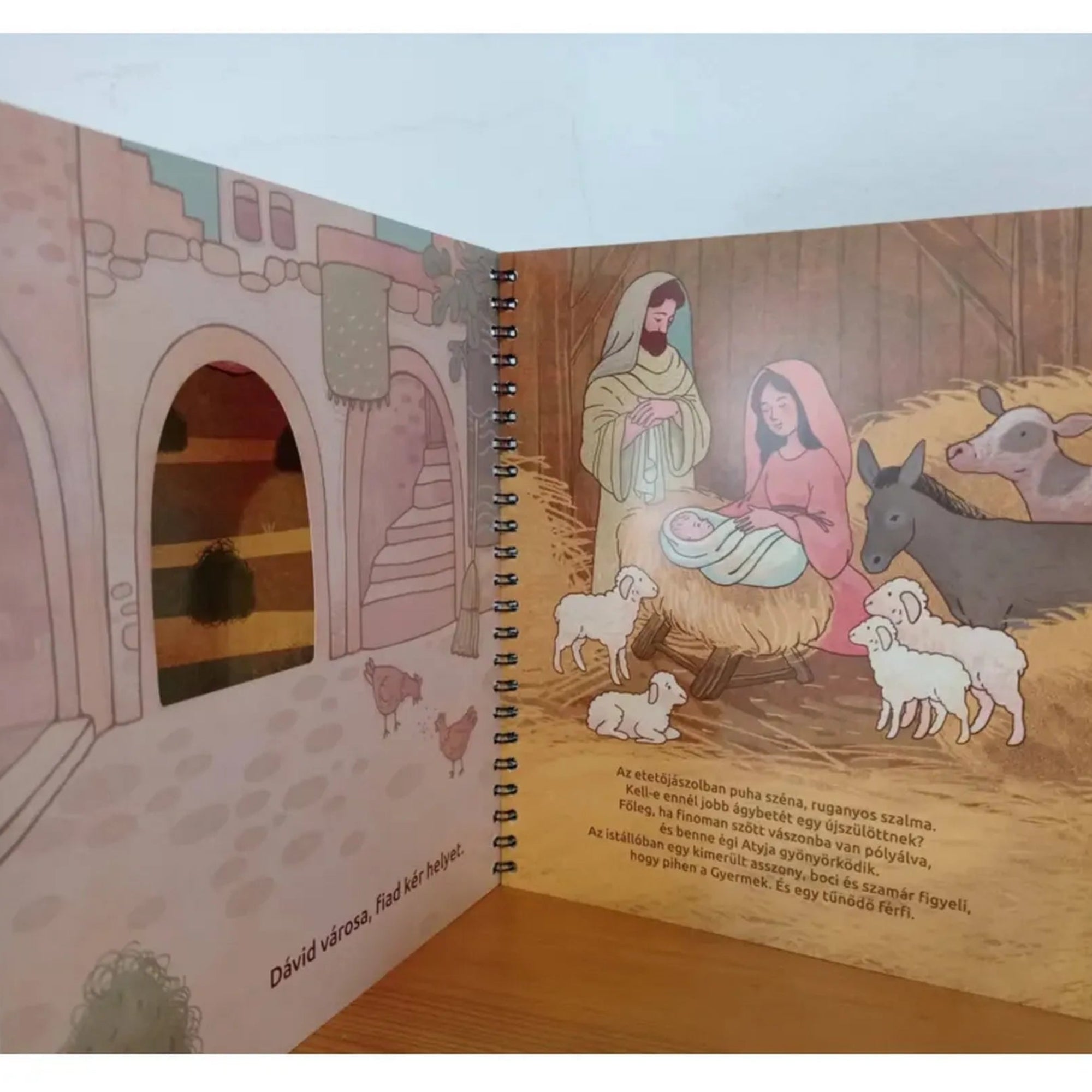 Az Ég és Föld Fia könyv betlehemi istállójelenete Józseffel, Máriával, a kis Jézussal, körülöttük báránnyal, ökörrel és szamárral.