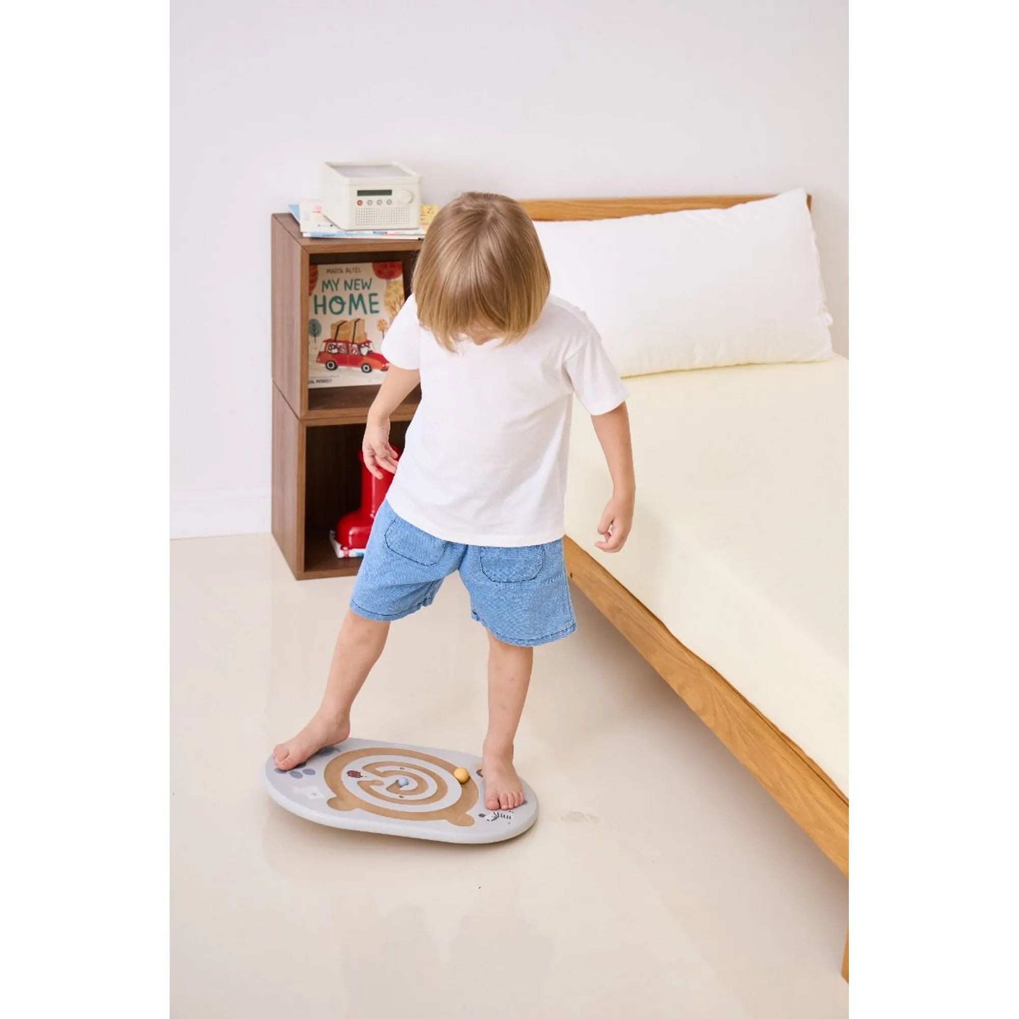 Gyermek a Viga egyensúlyozó és koordinációs táblán állva gyakorolja az egyensúlyt egy szobabelsőben.