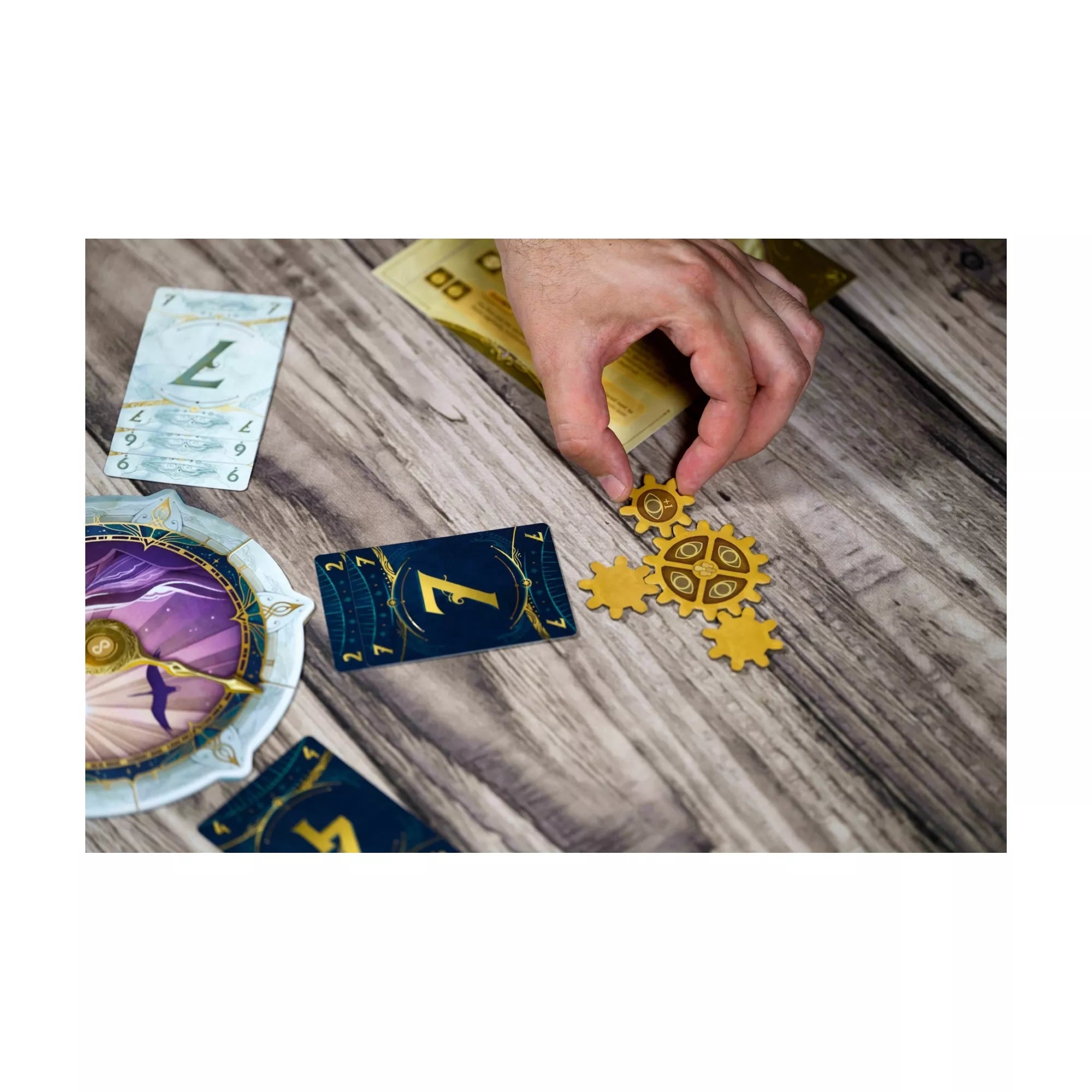 Közelkép egy játékos kezéről, amint arany színű fogaskerekeket illeszt a játéktérre az Időhurok társasjátékban, mellette sötétkék, misztikus kártyák.