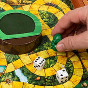 Közelkép a Jumanji társasjáték játéktáblájáról, amely dzsungel mintázatú, sárga ösvényekkel. Egy játékos keze zöld bábut helyez a pályára a dobókockák mellé, a középen található zöld Jumanji kupola mellett.