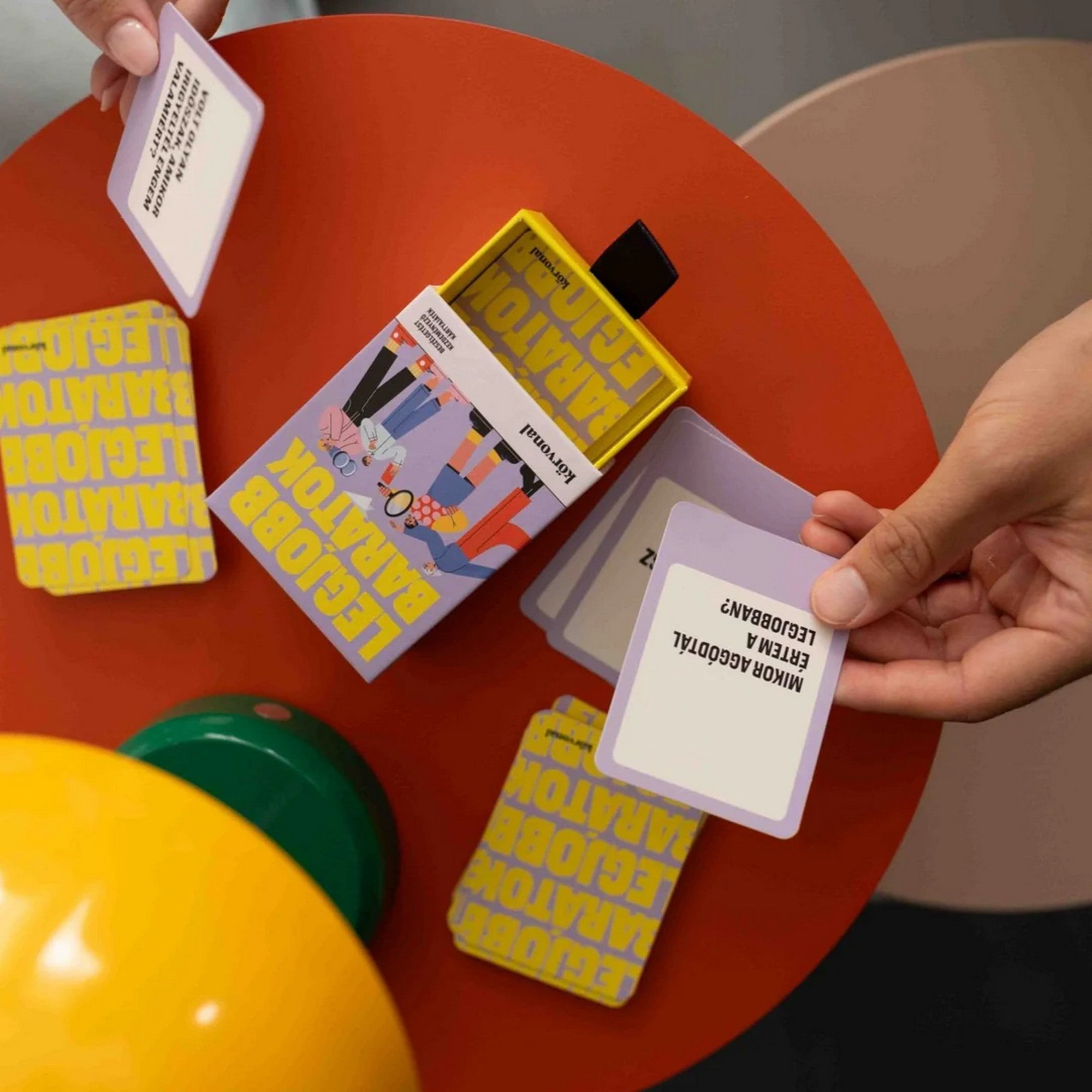 A nyitott Legjobb barátok játékkészlet látható: a dobozban a kártyapakli, néhány kártya felirattal felfordítva. Az egyik kártyán a „Mikor aggódtál értem a legjobban?” kérdés olvasható, ami jól tükrözi a játék érzelmi mélységét.