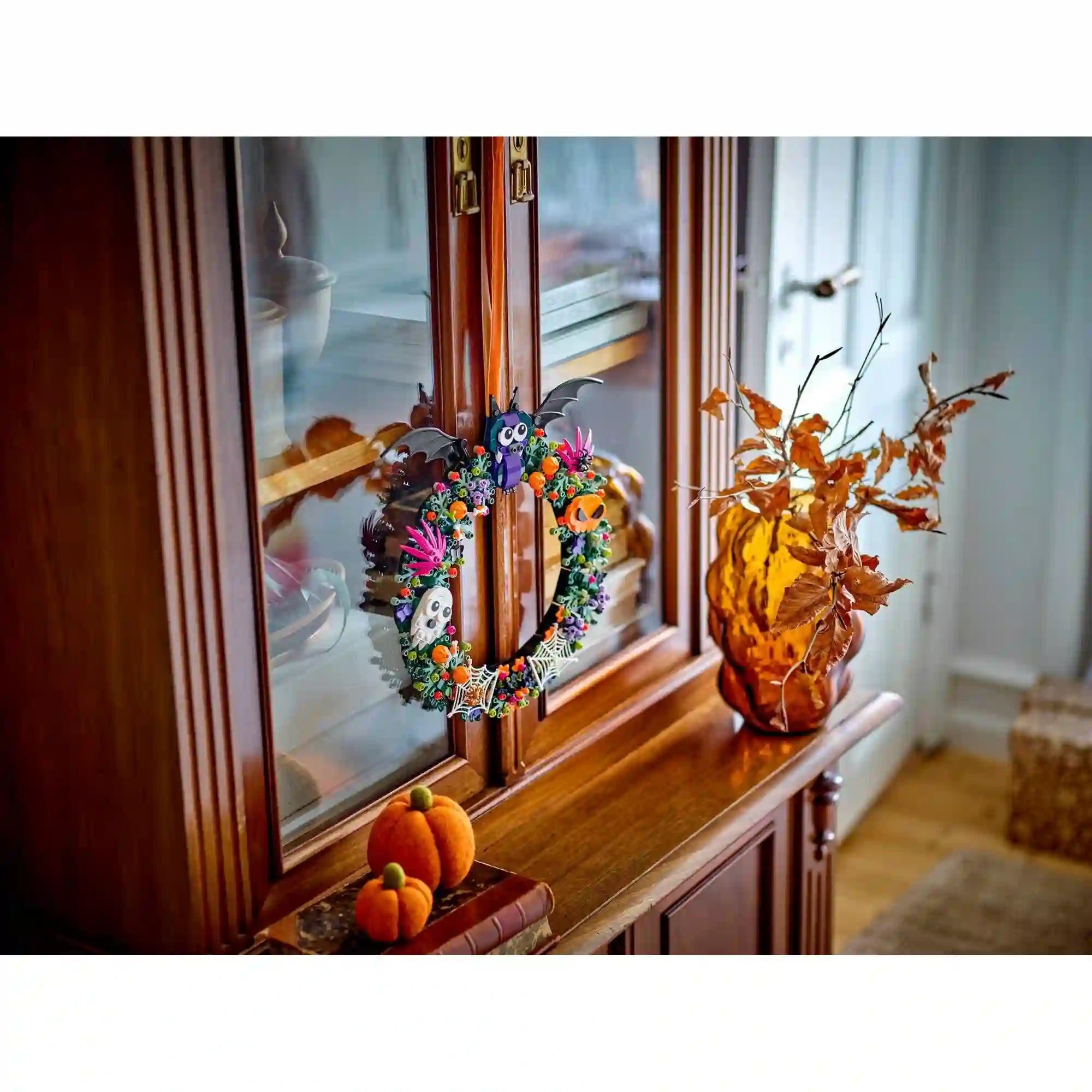 LEGO Halloweeni koszorú 40825 fa vitrines szekrényre akasztva, mellette őszi levelekkel díszített váza és két narancssárga tök.