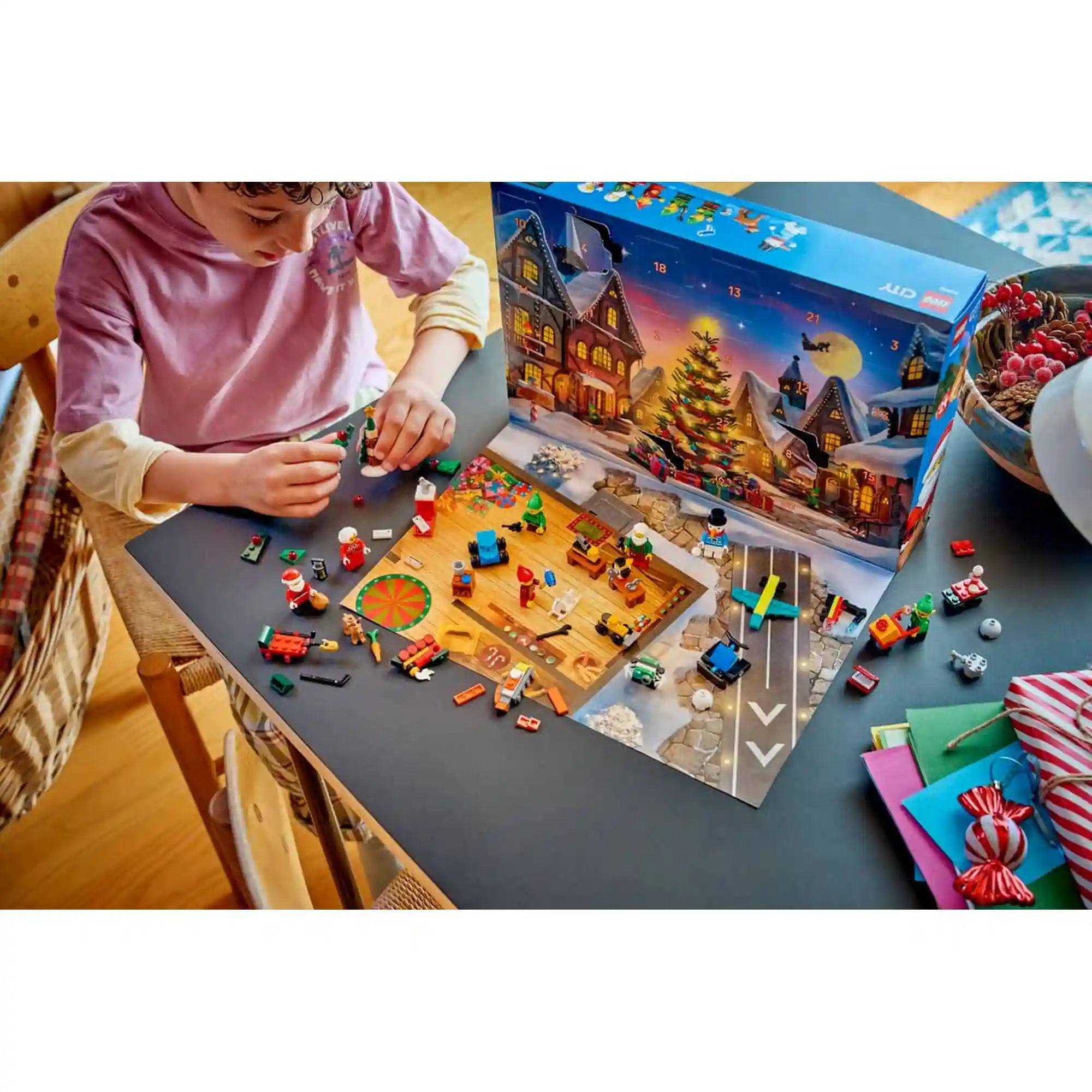 Gyermek építi a LEGO City: Adventi naptár 2026, 60510 apró karácsonyi modelljeit a kinyitott adventi naptár előtt.