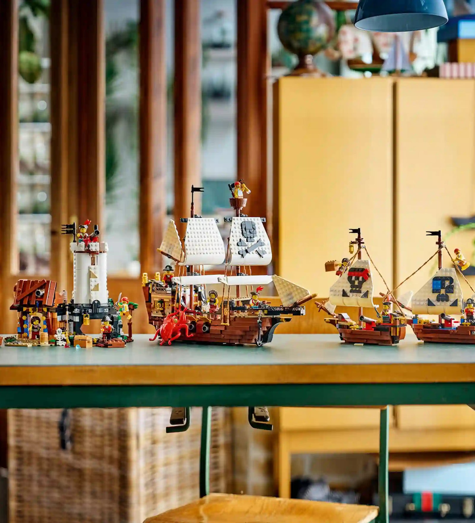 A LEGO Creator Ikonikus kalózhajó (31387) készlet mindhárom építési lehetősége egy asztalon. A jeleneten a kalózhajó, a kalózkastély és a két kisebb ikerhajó látható kalóz minifigurákkal és kiegészítőkkel.