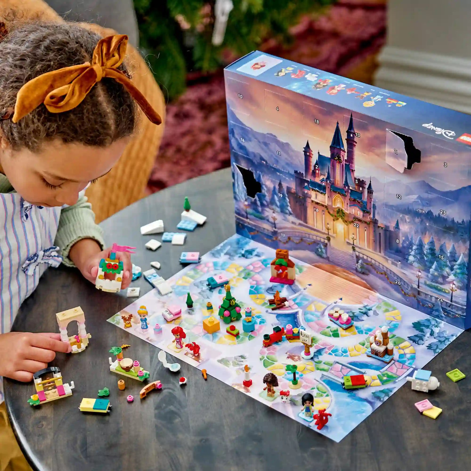 Masnis hajú kislány LEGO-építményt tart a kezében, előtte a kinyitott Disney adventi naptár és színes figurák az asztalon.