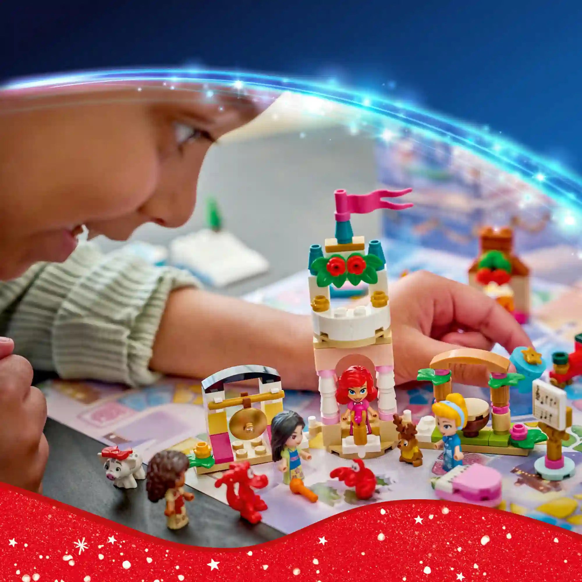 Kislány közelről nézi a LEGO Disney karácsonyi kastélyépítményt, körülötte hercegnők, állatfigurák és ünnepi kiegészítők.