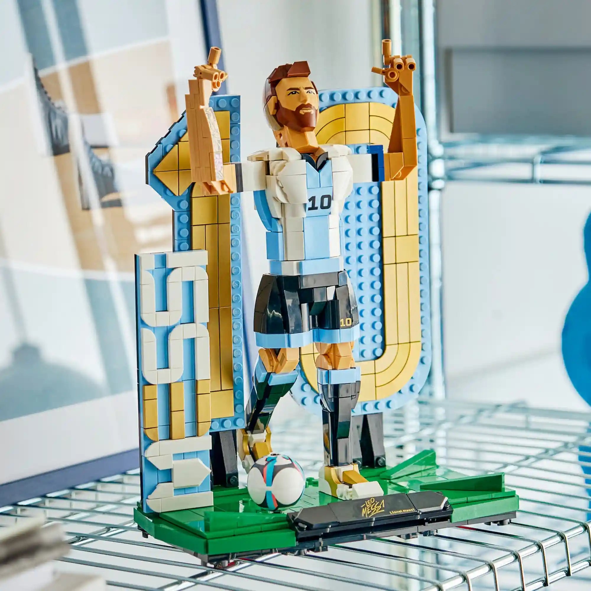 LEGO Lionel Messi – Futball-legenda (43015) kész kiállítási modell modern polcon elhelyezve, Messi győzelmi pózával, focilabdával és aranyszínű 10-es háttérelemmel.