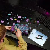 Egy gyermek építi a LEGO Fortnite Klombo lila szörnyét egy fekete asztalon, körülötte szétszórt elemek, minifigurák és egy tablet mutatja az útmutatót.
