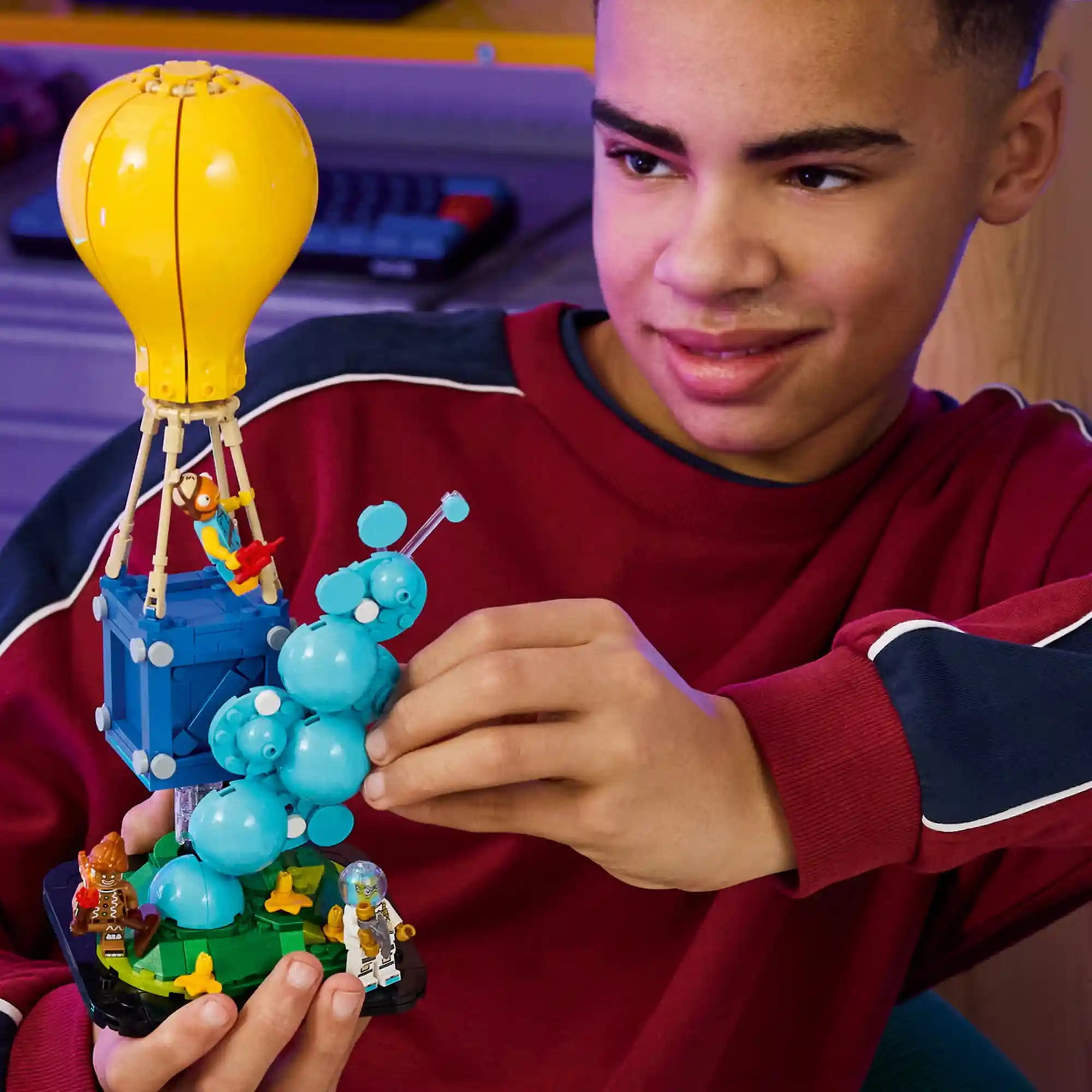Fiatal Fortnite rajongó kezében tartja a LEGO Fortnite Supply Drop modellt, amely a játék ikonikus ellátmányládáját ábrázolja.