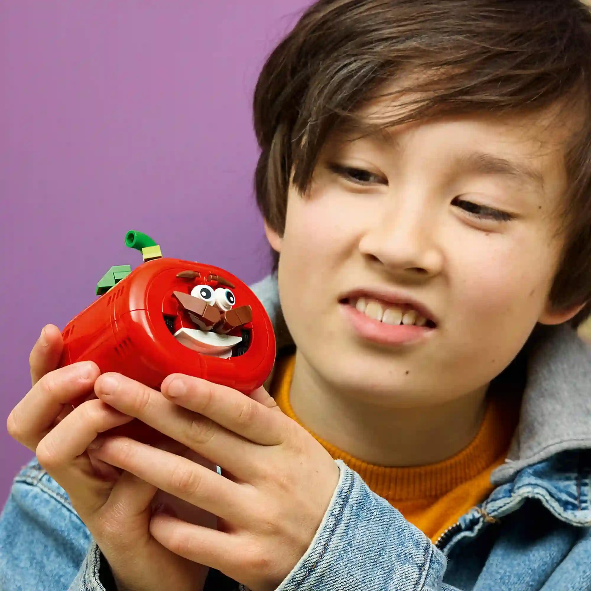Fiatal Fortnite rajongó kezében tartja a LEGO Fortnite Tomatohead figurát, bemutatva a karakter részletgazdag arcát és bajuszát.