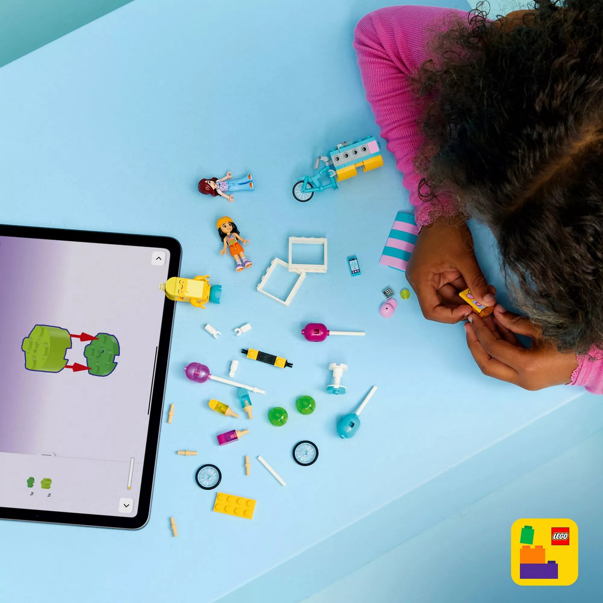 LEGO Friends Jégkrémes és lufis stand (42692) építőjáték elemei játék közben, szétszórt kiegészítőkkel, minifigurákkal és egy tablettel, amely digitális építési útmutatót mutat.