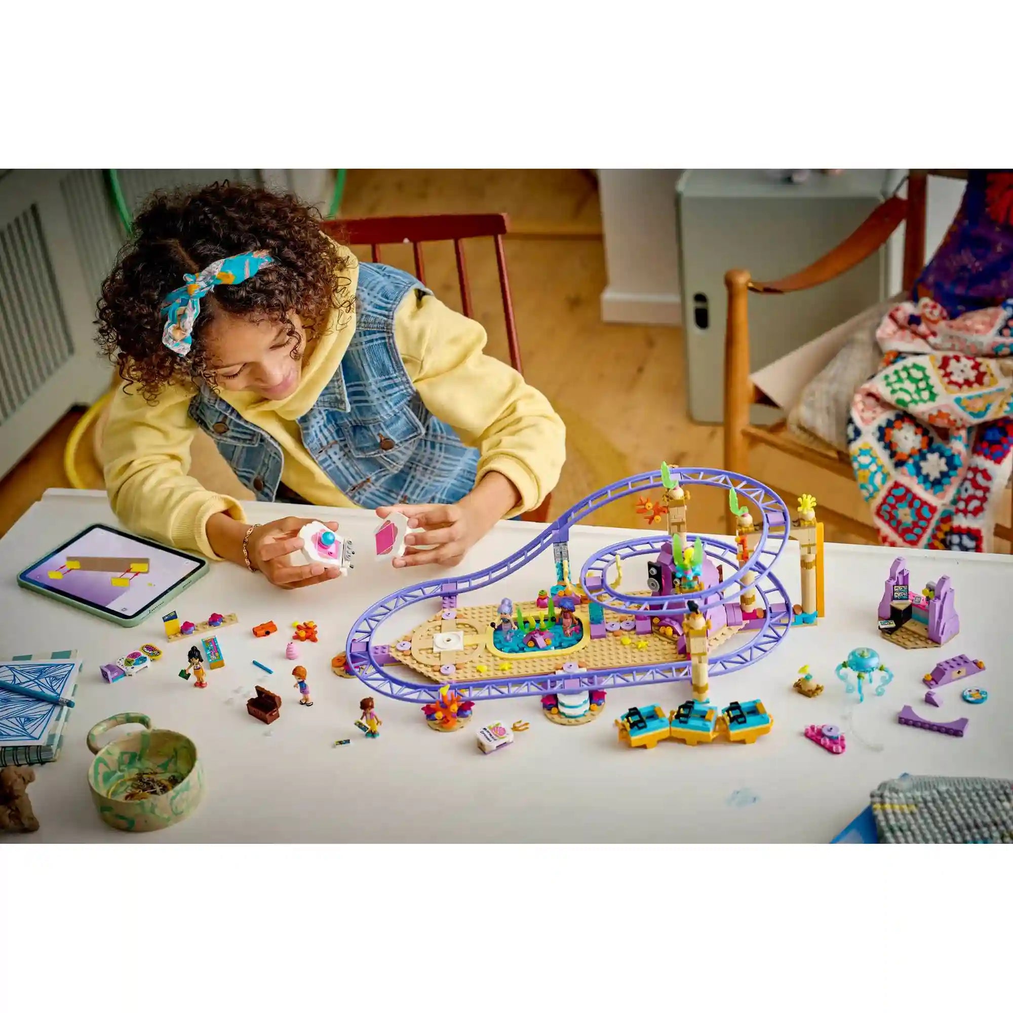 LEGO Friends: Hableányos hullámvasút 42703, 864 darabos készlet építési jelenete, a szétszedett elemekkel, figurákkal és a részben összeállított hullámvasút pályával.