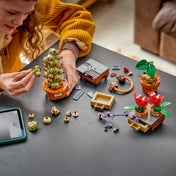 Gyermek építi a LEGO Harry Potter Roxforti gyógynövénytan növényei (76474) készletet. Az asztalon szétszedett elemek, a Mimbulus mimbletonia növény, a mandragóra, a harapós muskátlik és az építési folyamat részletei láthatók.