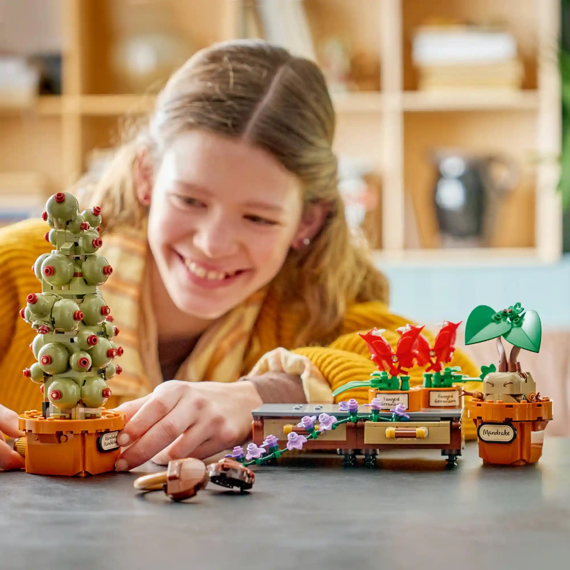 Mosolygó gyermek játszik a LEGO Harry Potter Roxforti gyógynövénytan növényei (76474) készlettel. Az előtérben a Mimbulus mimbletonia növény, a harapós muskátlik és a mandragóra modell látható a Roxfort gyógynövénytan óráit idéző hangulatban.