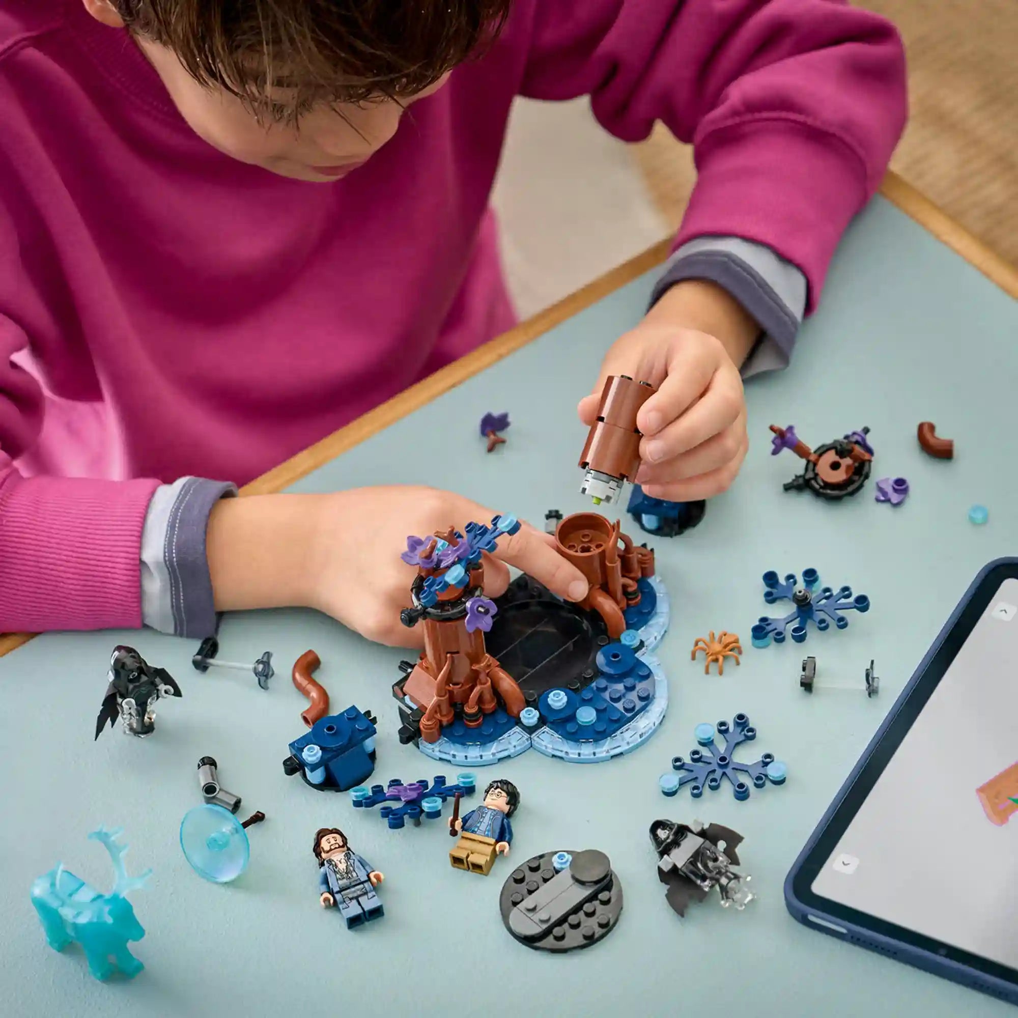 Gyermek építi a LEGO Harry Potter A Tiltott Rengeteg: Expecto Patronum készletet, miközben a LEGO Builder alkalmazás digitális útmutatóját használja.