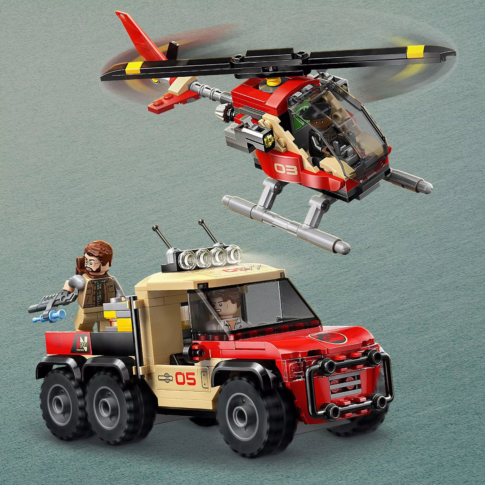 „LEGO Jurassic World (76976) járművek akcióban: a vörös-sárga helikopter a levegőben repül, alatta pedig a masszív, hatkerekű terepjáró halad előre, benne egy minifigurával. A jelenetben egy másik minifigura is látható, aki egy kék lövedékkel felszerelt kábítófegyvert tart, készen az expedícióra.