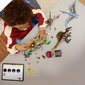 „A LEGO Spinosaurus és Quetzalcoatlus légi küldetés (76976) elemei szétszórva az asztalon, köztük dinoszaurusz figurák, templom, helikopter, terepjáró és minifigurák, építés közben táblagépes útmutatóval.”