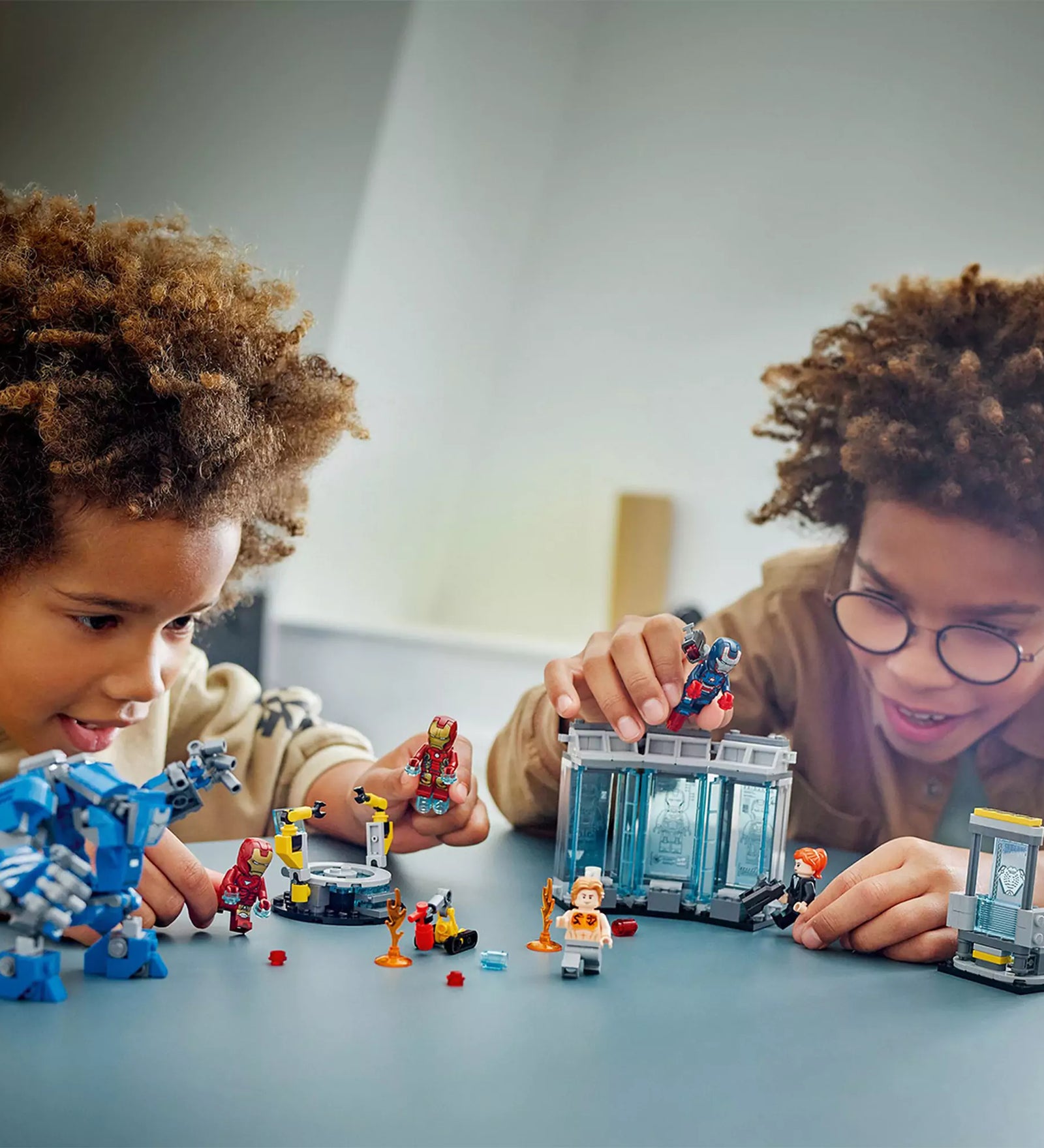 Két gyerek játszik a LEGO Marvel A Vasember laboratóriuma: páncélcsarnok készlettel egy asztalon.