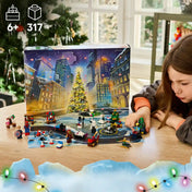 Kislány Marvel LEGO figurákkal játszik a kinyitott adventi naptár előtt, havas városi háttérrel és karácsonyfával.