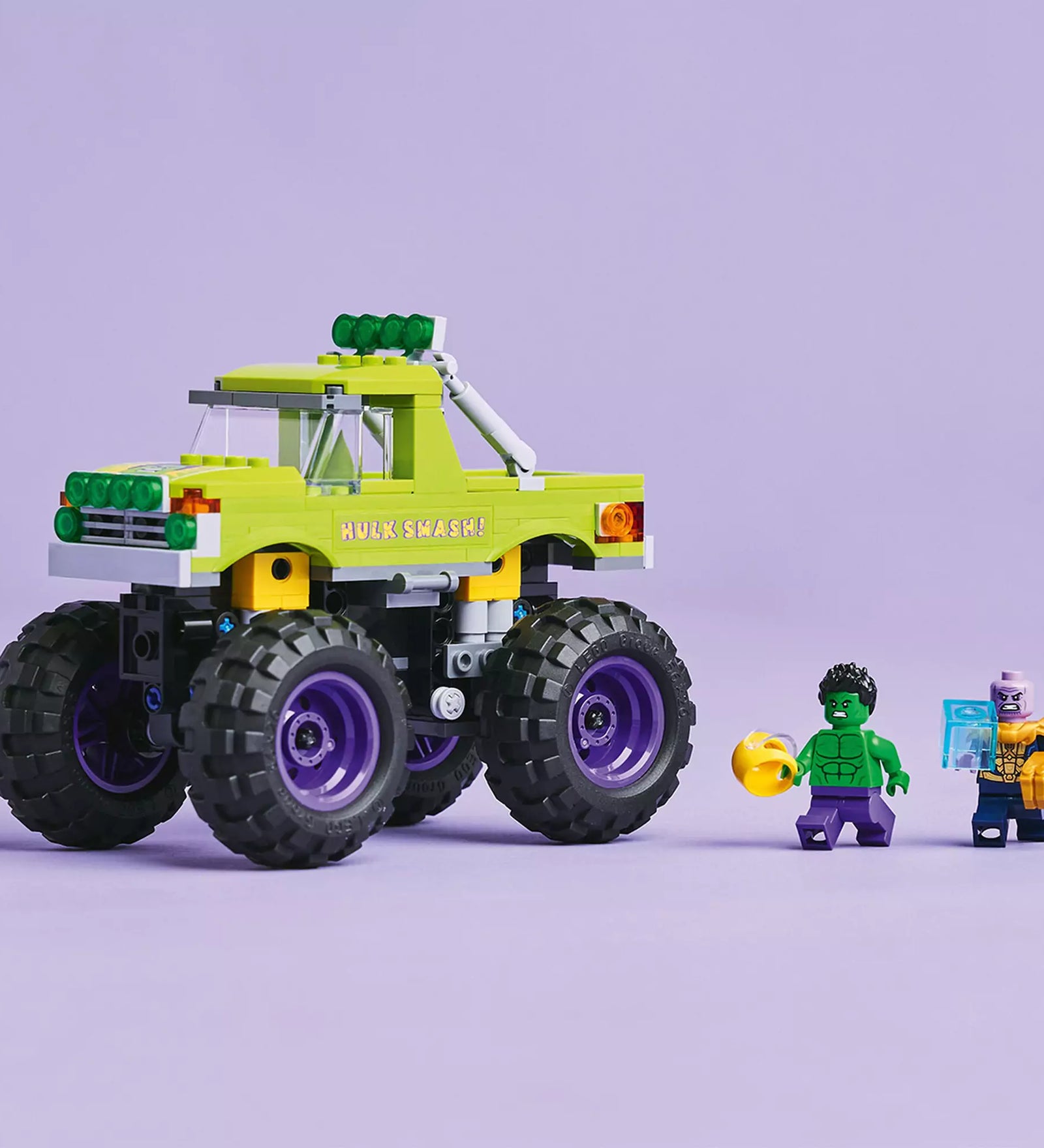 LEGO Marvel Hulk óriási terepjárója vs. Thanos terepjáró és minifigurák, köztük Hulk és Thanos, lila háttér előtt.