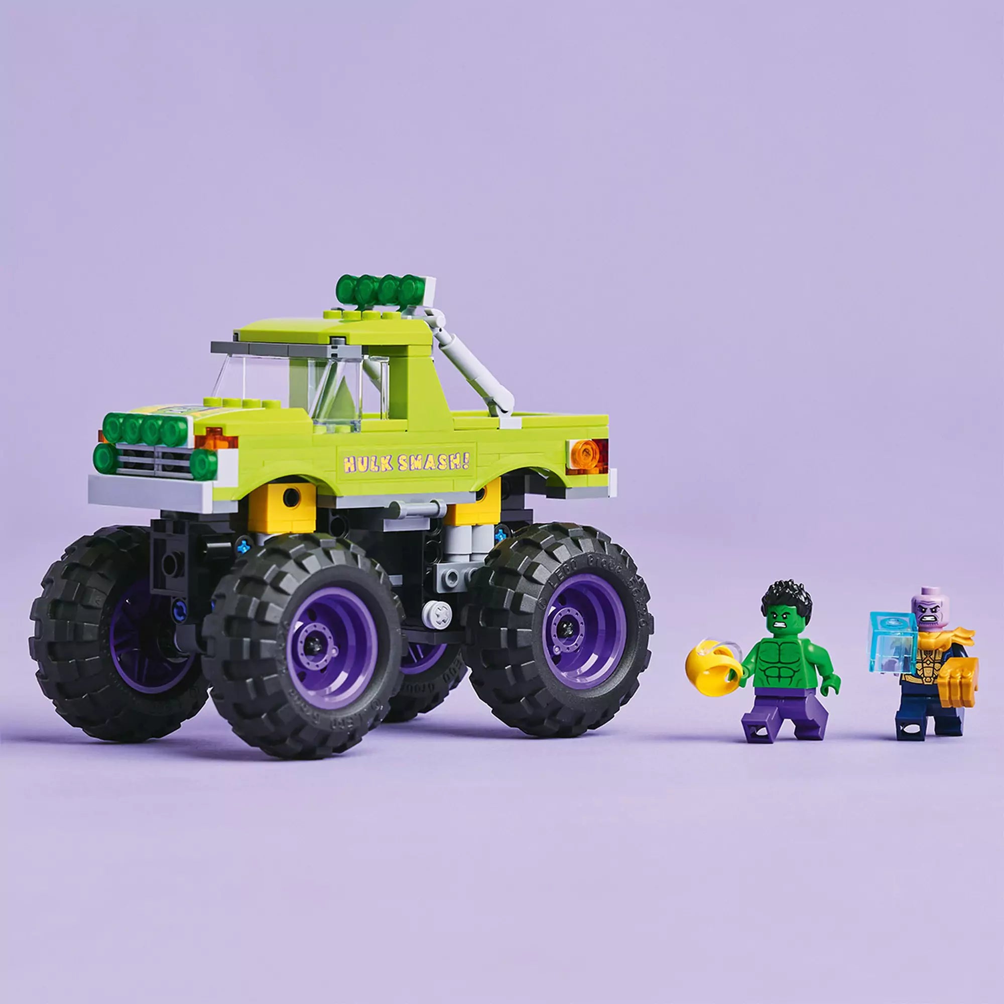 LEGO Marvel Hulk óriási terepjárója vs. Thanos terepjáró és minifigurák, köztük Hulk és Thanos, lila háttér előtt.