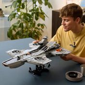 Sárga pólós férfi a LEGO Marvel Helicarrier megépített modelljét tartja egy asztal fölött.