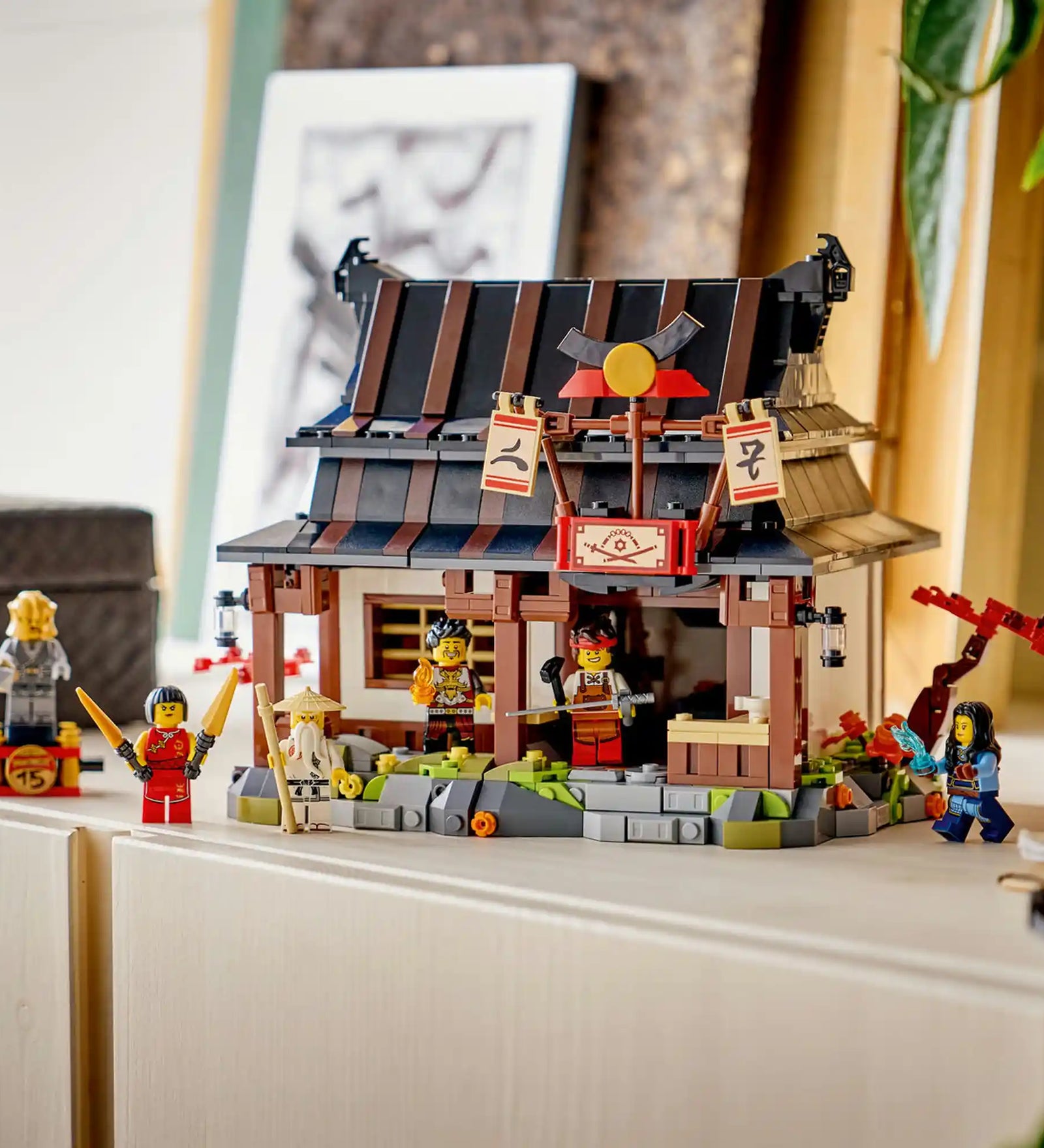 LEGO NINJAGO: Négy Fegyver Kovácsműhely, 15. évforduló készlet megépített kovácsház épülettel és minifigurákkal kiállítva polcon.