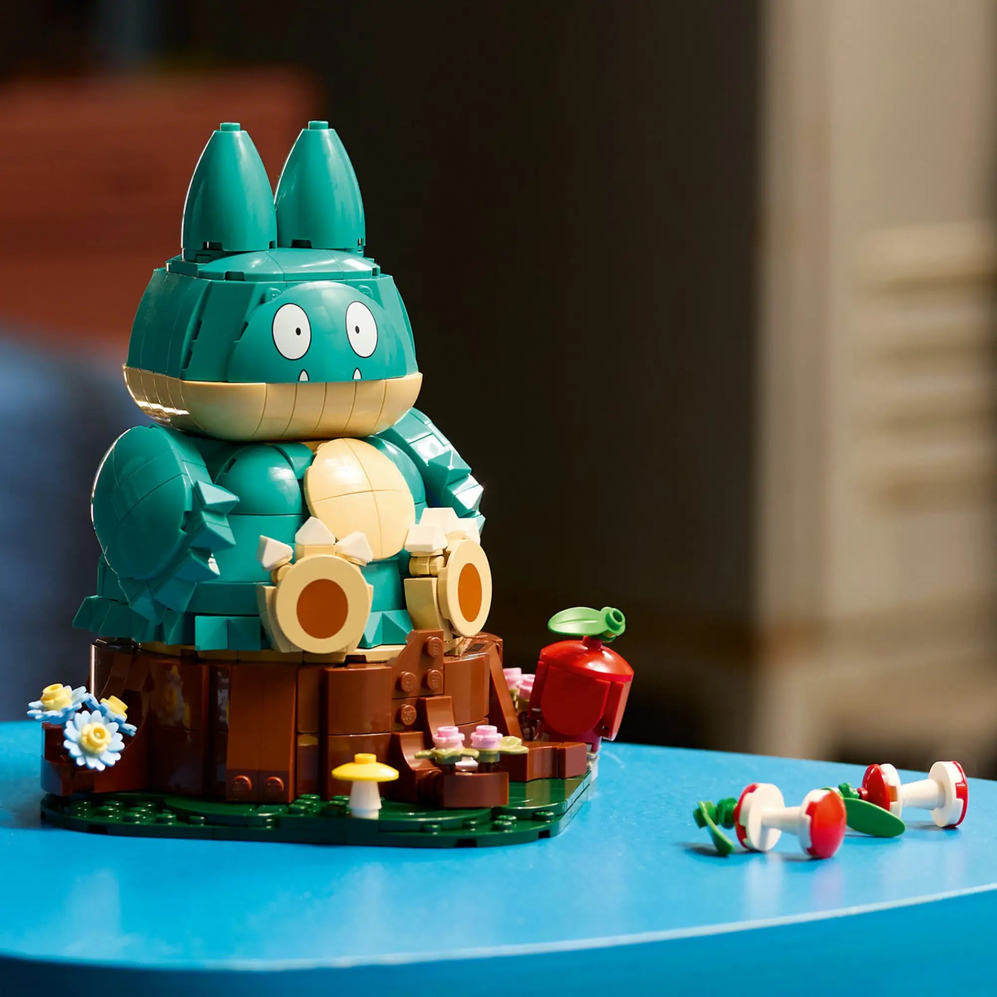 A megépített LEGO Pokémon Munchlax figura kiállítva almával, virágokkal és gombákkal díszített talapzaton.