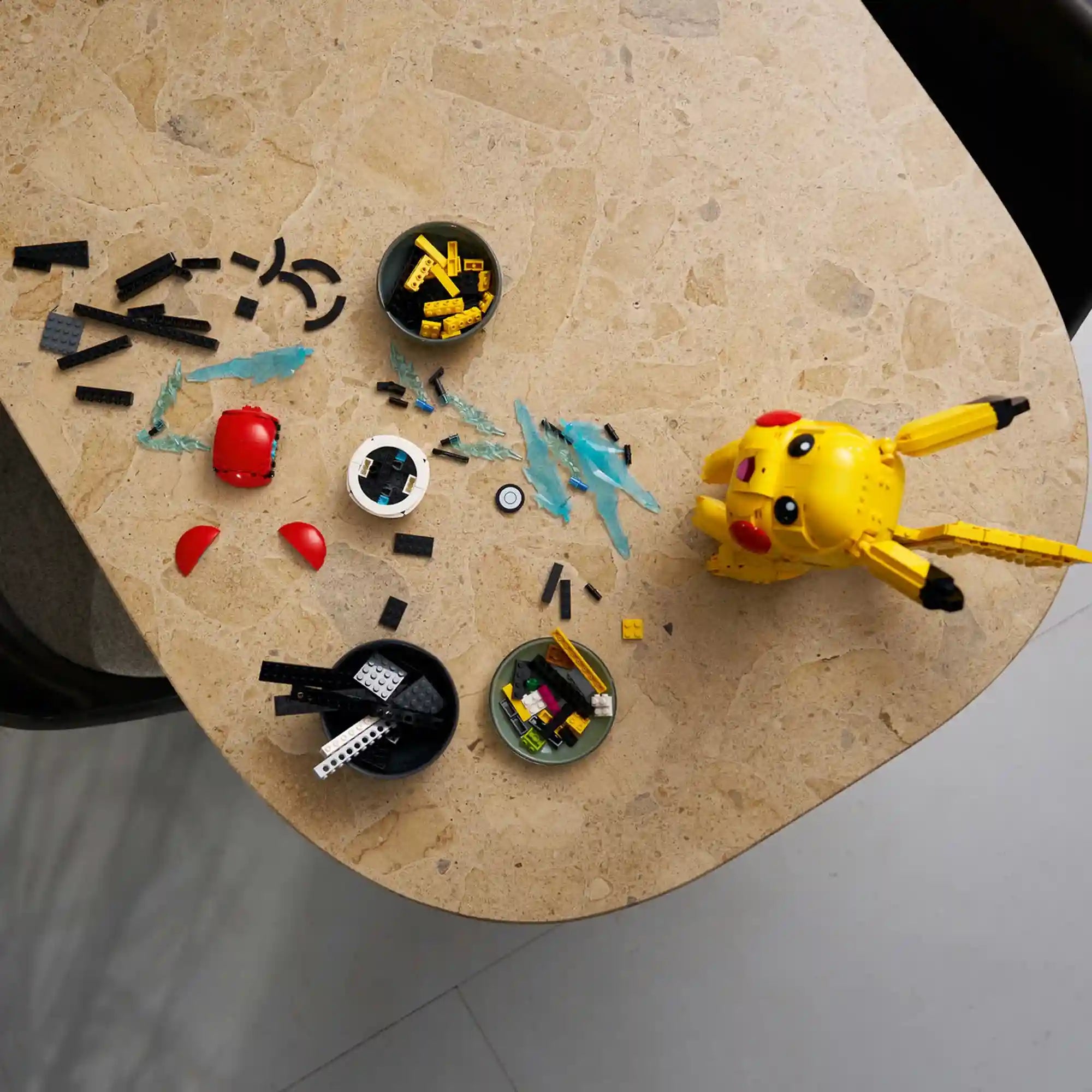 LEGO Pokémon: Pikachu és pokélabda 72152, 2050 darabos alkatrészek felülről, szétszórt LEGO elemekkel, Pikachu fejjel és építési folyamat közben.
