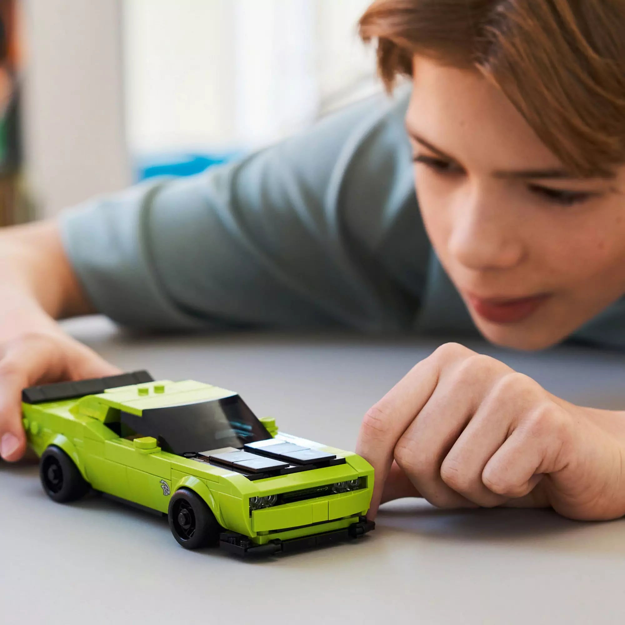 Gyerek játszik a LEGO Dodge Challenger SRT Hellcat (77237) modellel, az autó asztalon gurul.