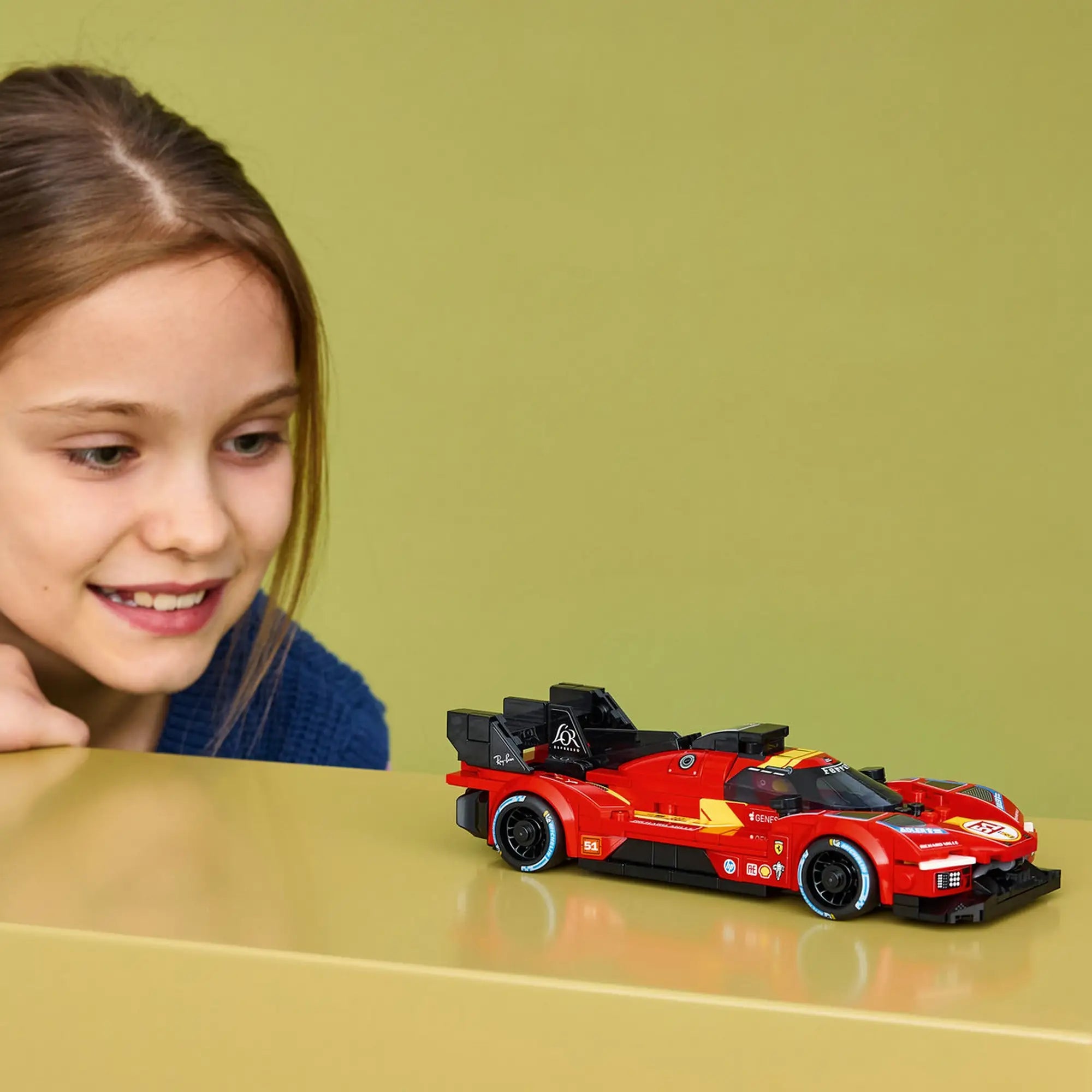 Kislány figyeli a LEGO Speed Champions Ferrari 499P (77261) piros versenyautó modelljét egy asztalon.