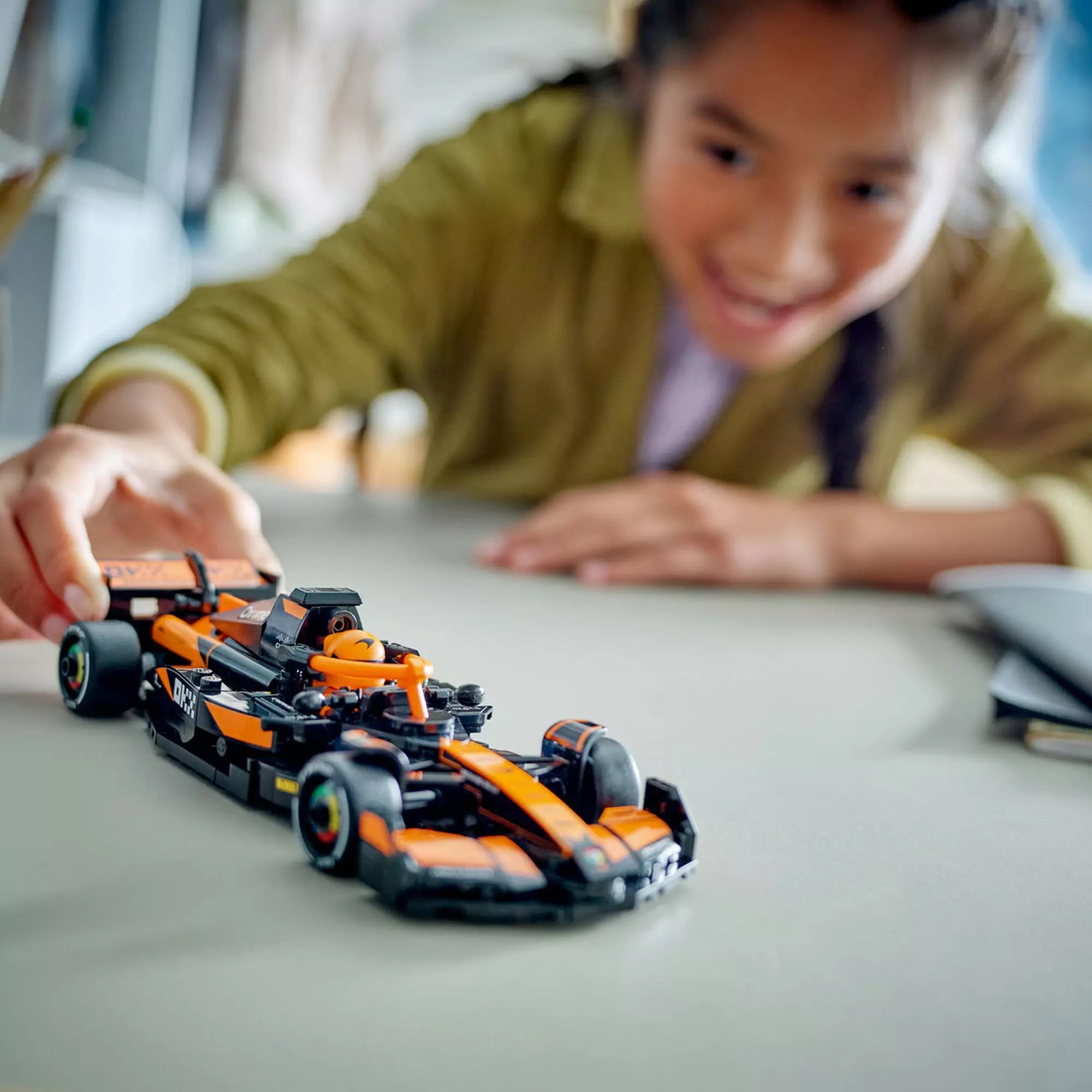 Egy gyerek játszik a LEGO Speed Champions McLaren F1 Team MCL38 versenyautóval, izgatott arckifejezéssel.