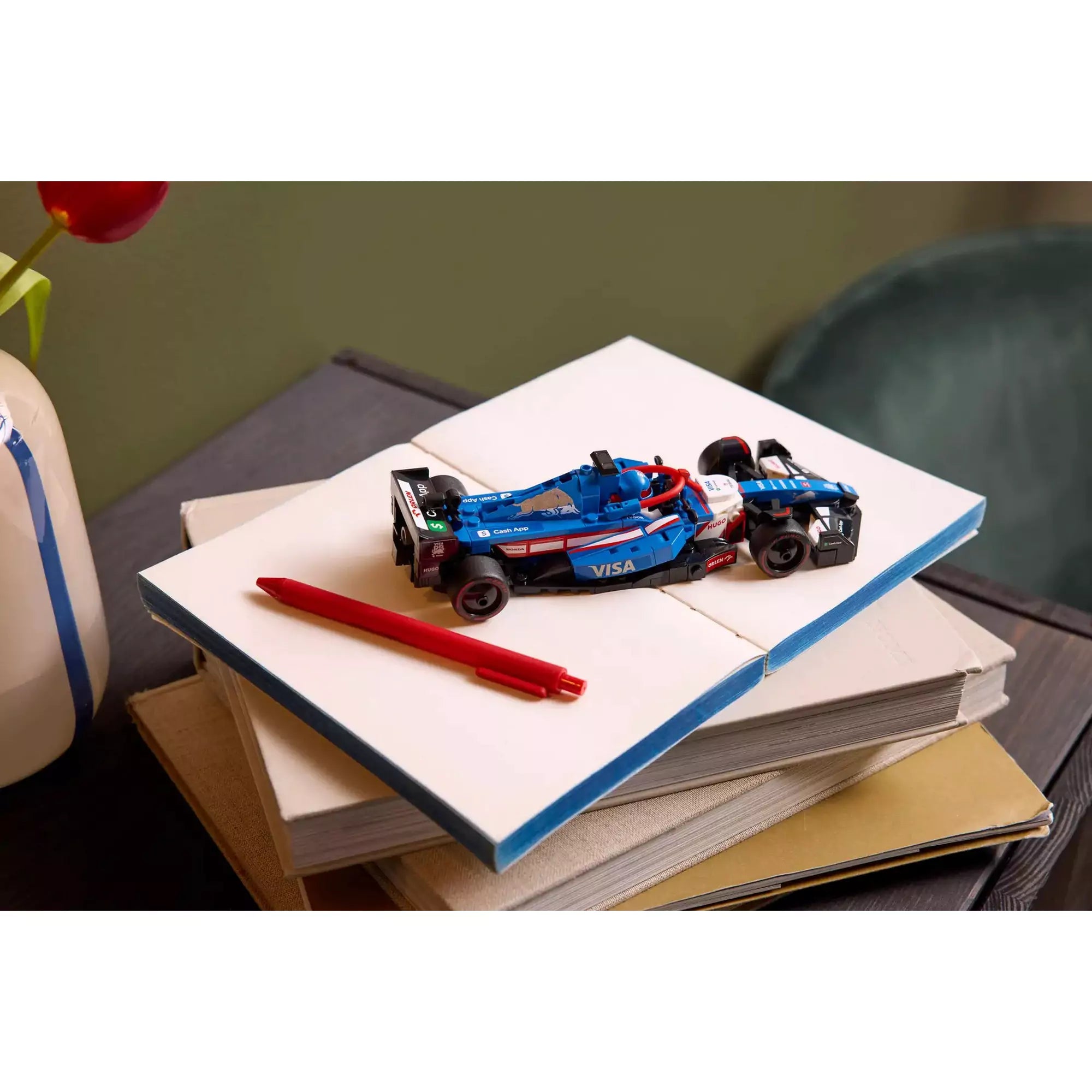 A LEGO Speed Champions Visa Cash App RB VCARB 01 F1 versenyautó 77246 kiállítva könyveken, piros tollal mellette.