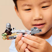 Gyermek kezében tartott LEGO Star Wars speeder bike, rajta a Mandalorian minifigurával és Grogu figurával, valós játékhelyzetben bemutatva.