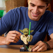 Egy felnőtt játékos építi a LEGO Star Wars Yoda modellt, asztalon elhelyezve, mellette a minifigura.