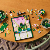 A LEGO Wicked Emerald City falikép részben megépített állapotban egy faasztalon. Körülötte tálkákban és szétszórva a készlet építőelemei, valamint néhány minifigura. A modell felső része már elkészült, rajta az Emerald City tornyai.
