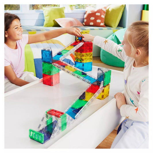 Két mosolygó gyerek épít és játszik a MAGNA-TILES Rail Racers Deluxe mágneses pályával. A színes elemekből készült pályán golyókat indítanak el, miközben közösen alkotnak és tanulnak.