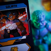 Marvel United: Polgárháború magyar nyelvű kiegészítő Goliath karakterkártyája a hozzá tartozó figura elmosódott hátterével.
