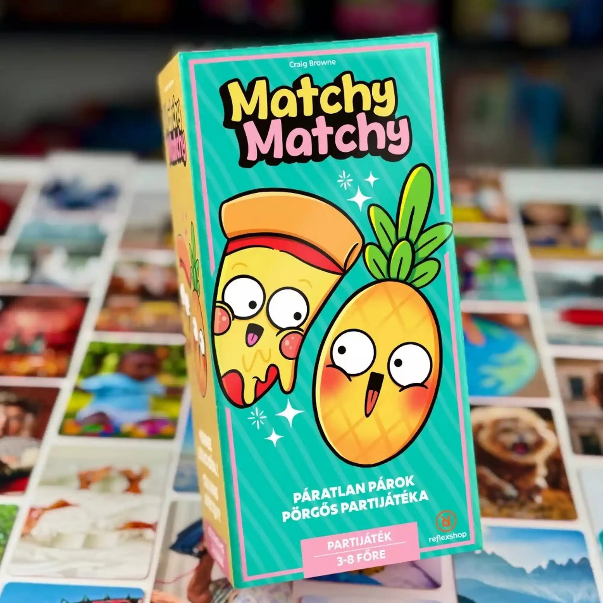 Matchy Matchy magyar nyelvű társasjáték doboza a játék fényképes kártyáival a háttérben.