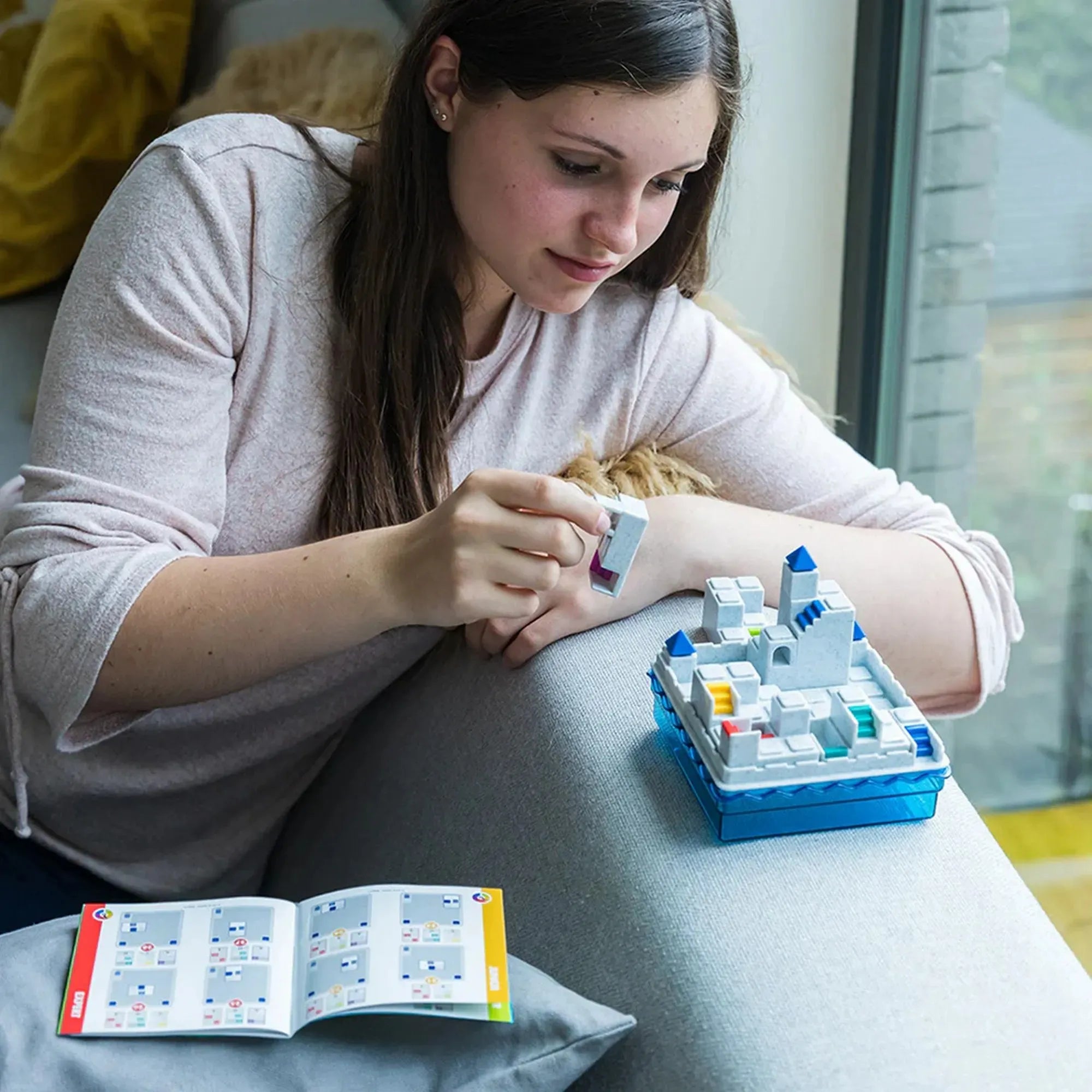 Egy lány a kanapén ülve logikai feladványt old meg az Atlantis Escape játékkal, a tábla és a füzet előtt.