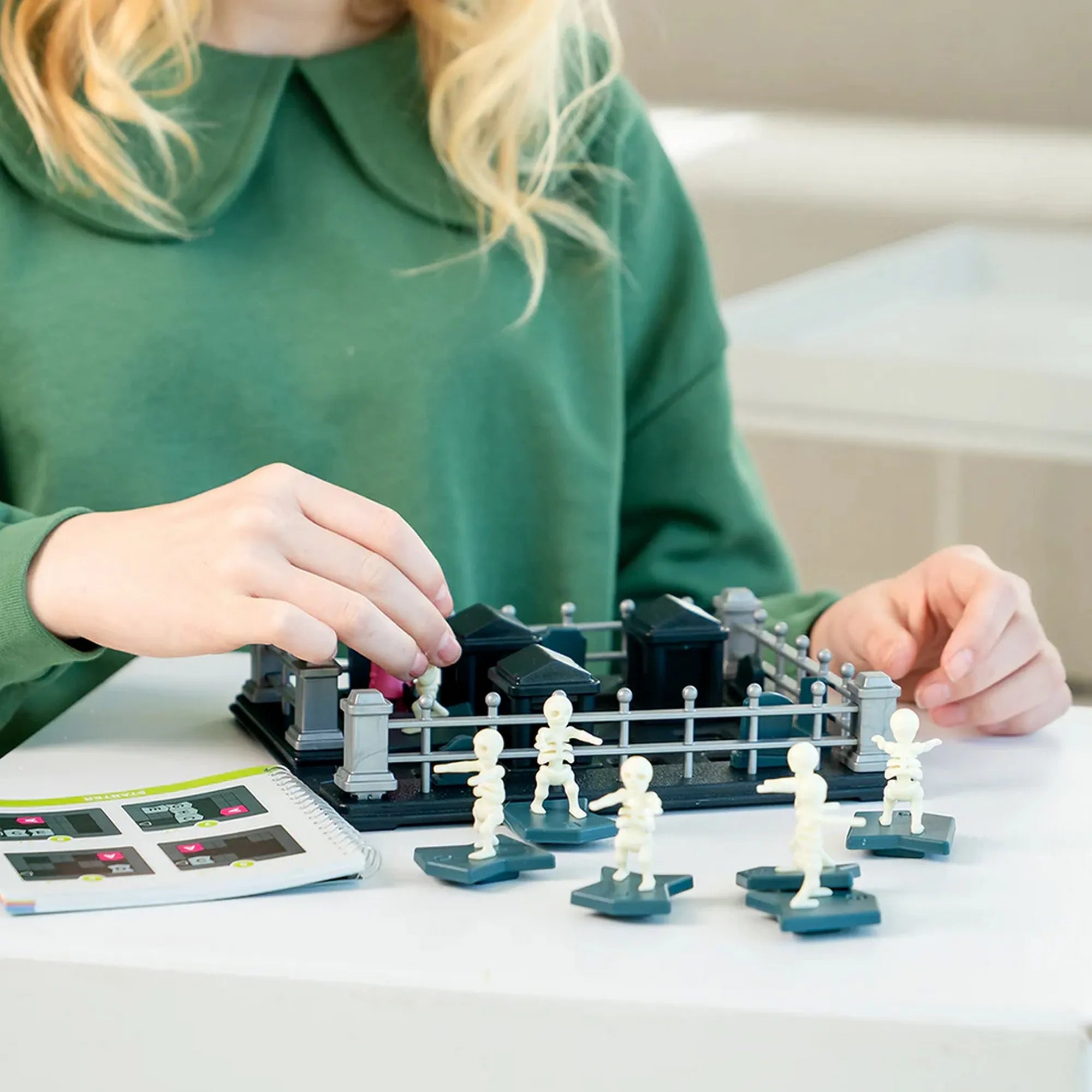 Egy gyerek a Smart Games Graveyard Shift logikai játék pályáján mozgatja a szellemes csontvázfigurákat és akadályokat.