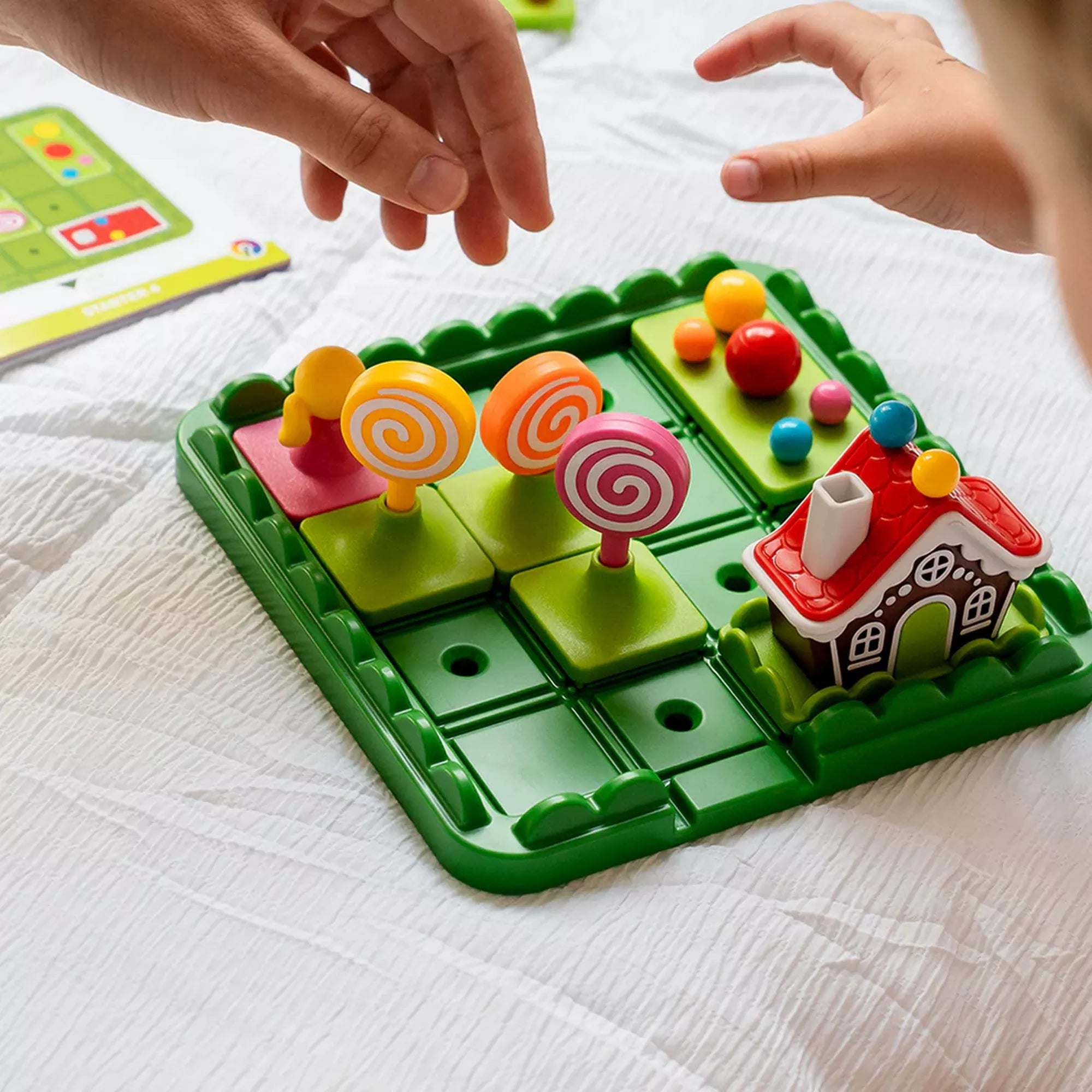 „A Hansel & Gretel Deluxe játék használat közben, a gyerek keze a színes cukorkaút és a nagy nyalókaelemek mellett.”