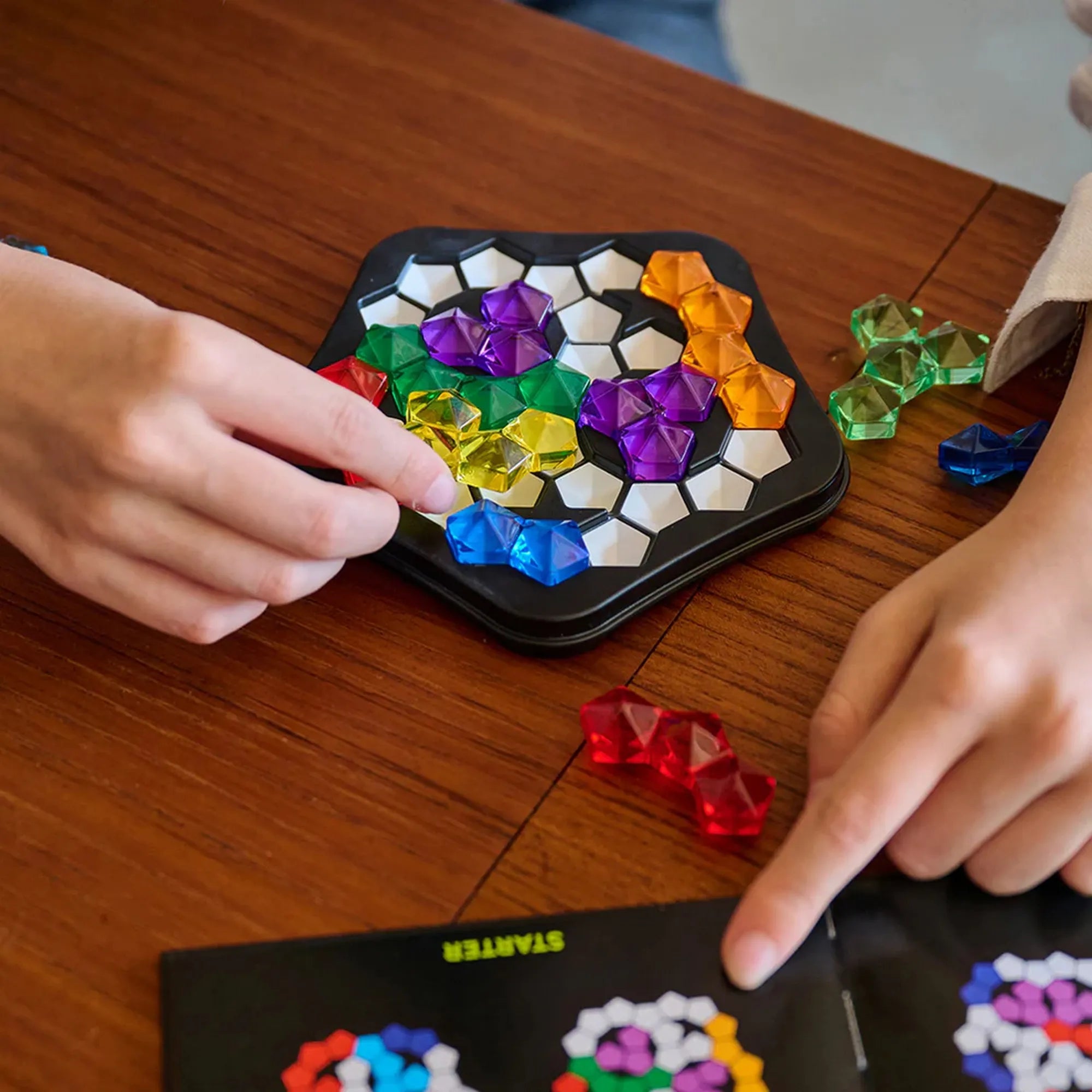 IQ Pentagon logikai játék részlet, kézben tartott színes elemek és a játéktábla a feladatmegoldás közben.