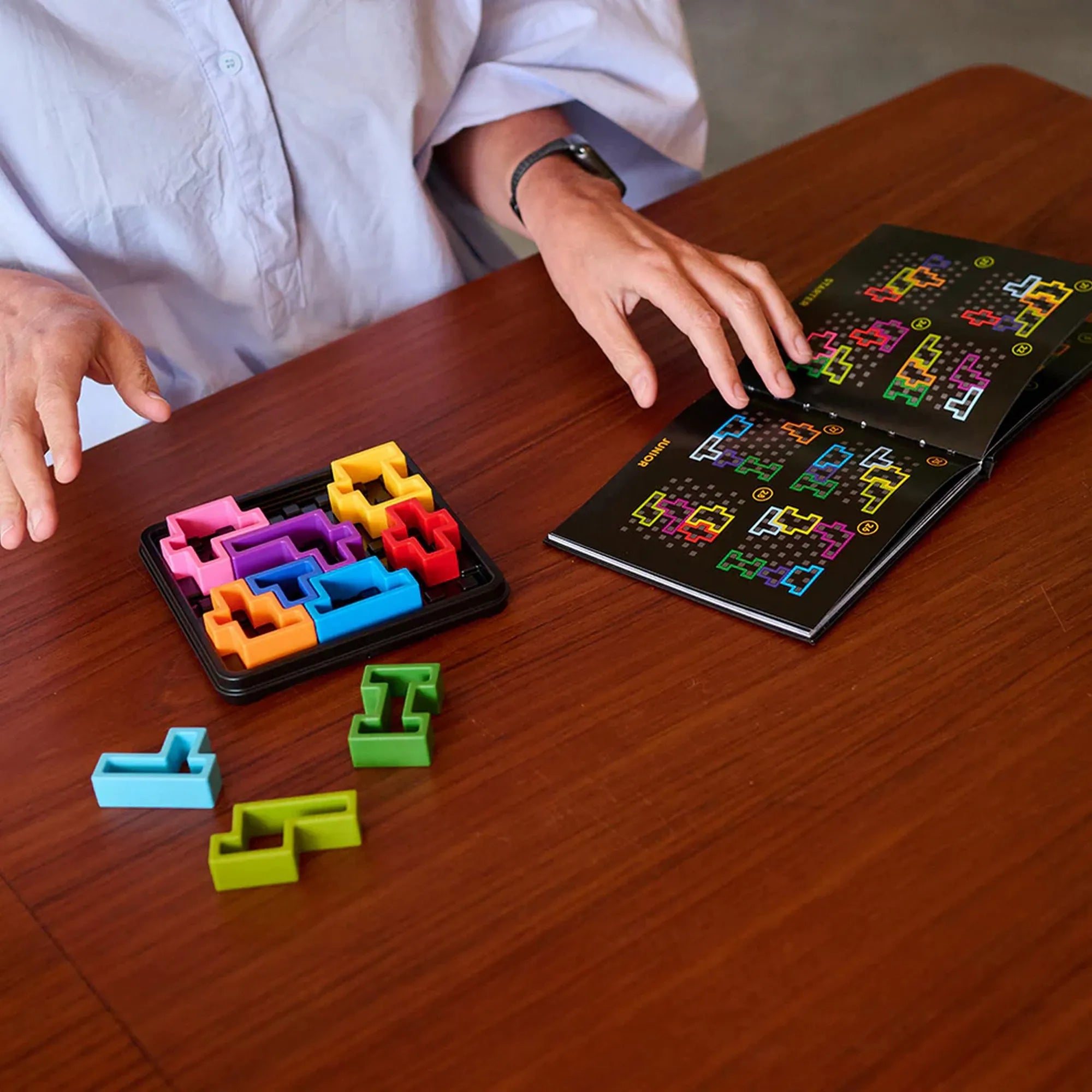 IQ Square logikai játék használat közben, kirakóelemek és kihívásfüzet az asztalon.