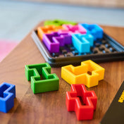 IQ Square logikai játék színes elemei közelről, kirakó darabok a játéktábla előtt.