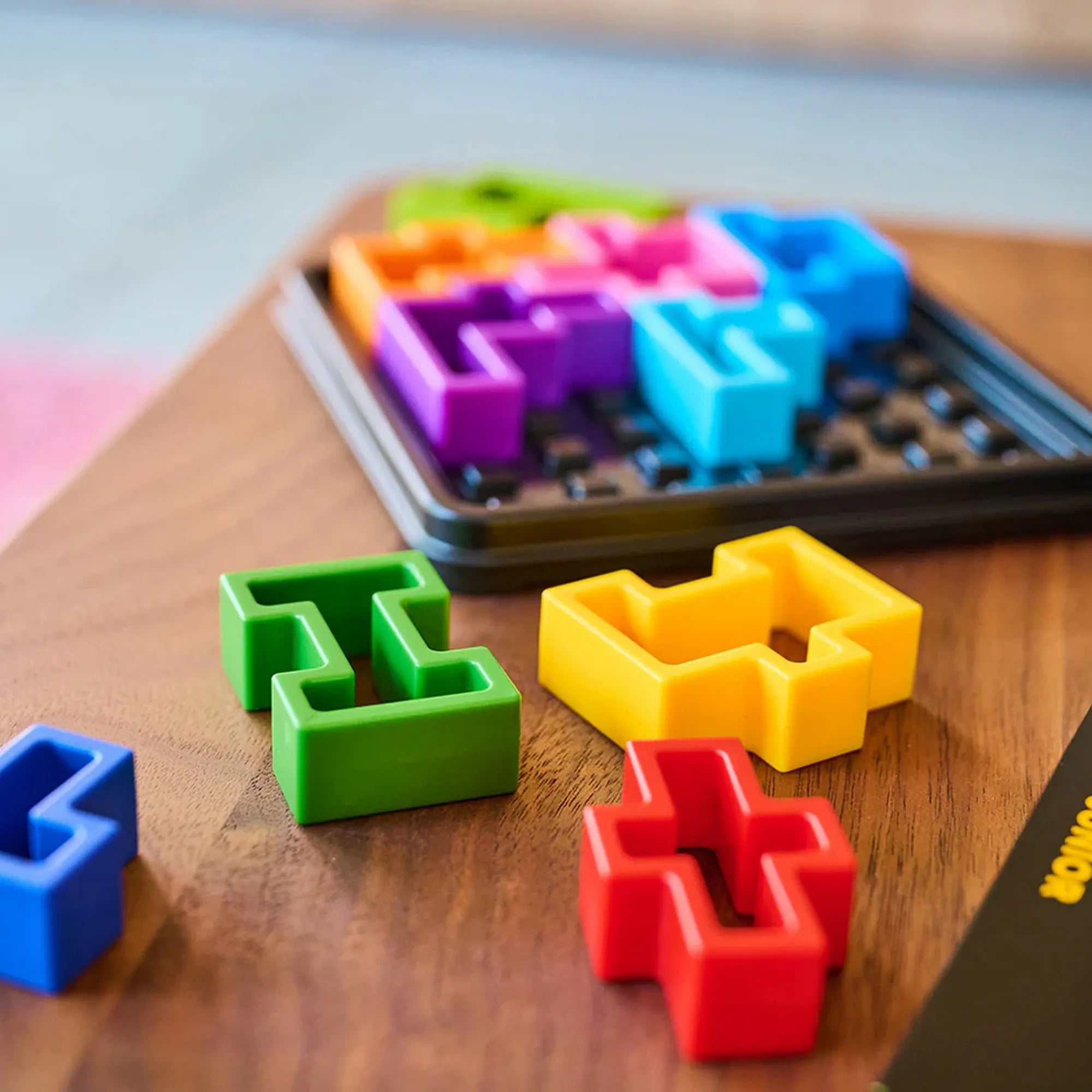 IQ Square logikai játék színes elemei közelről, kirakó darabok a játéktábla előtt.