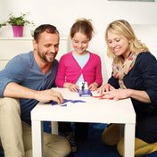 „Család Tangoes Starter játékkal játszik, a gyerek és a szülők tangram elemekből próbálják kirakni a kártyán látható alakzatot.”