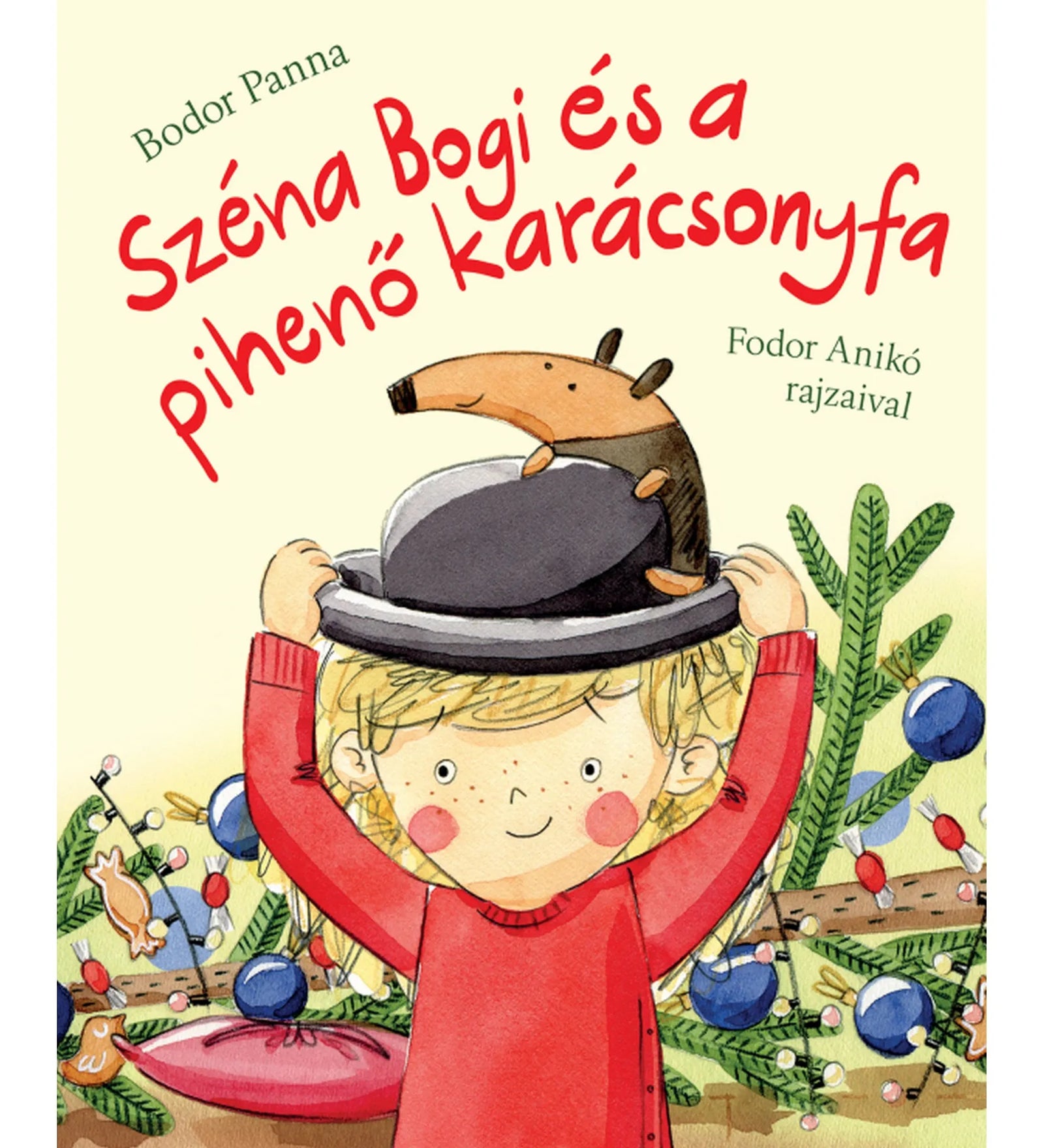 A „Széna Bogi és a pihenő karácsonyfa” című könyv borítója: egy mosolygós kisgyermek piros pulóverben kalapot tart a fején, amelyen egy kedves kis hangyaorrú állat ül. A háttérben karácsonyi díszek és fenyőágak láthatók, ünnepi, vidám hangulatot árasztva.