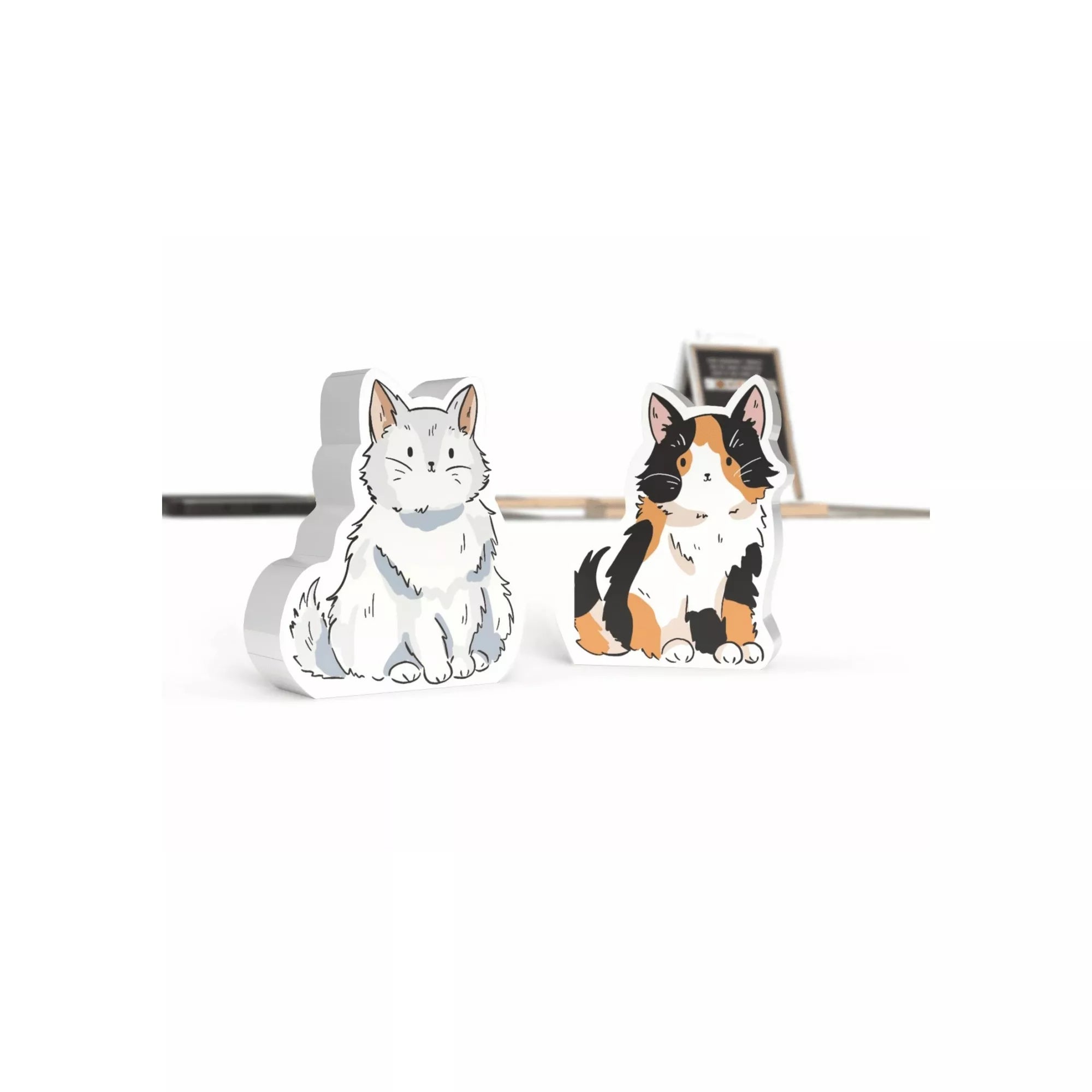 Két aranyos macskafigura a Virágvásár társasjátékból: egy fehér és egy háromszínű cica. A fafigurák részletesen illusztráltak, a háttérben a játék táblája halványan látható.